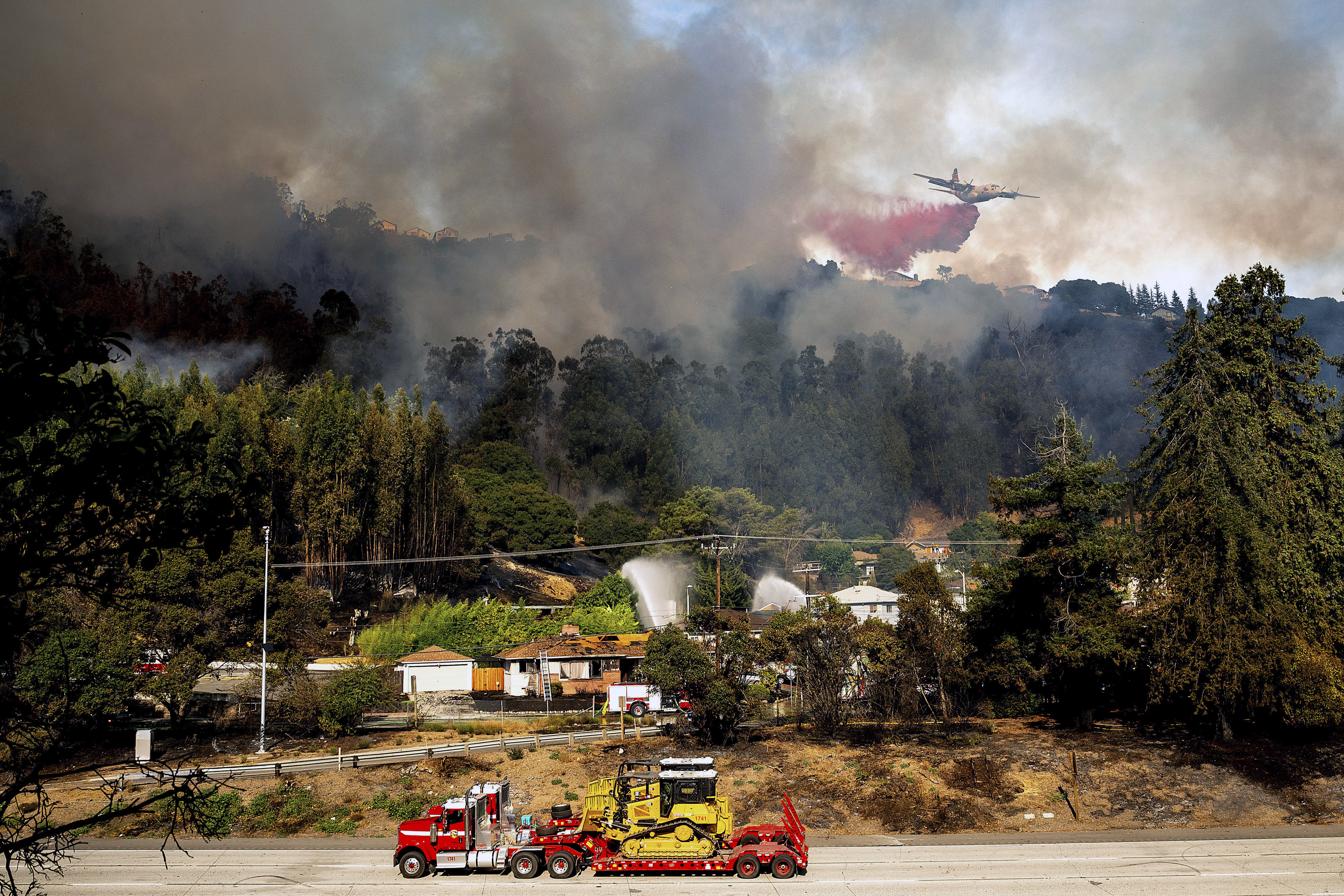 An air tanker drops retardant on a grass fire burning above Interstate 580 in Oakland, Calif., Friday, Oct. 18, 2024. (AP Photo/Noah Berger)