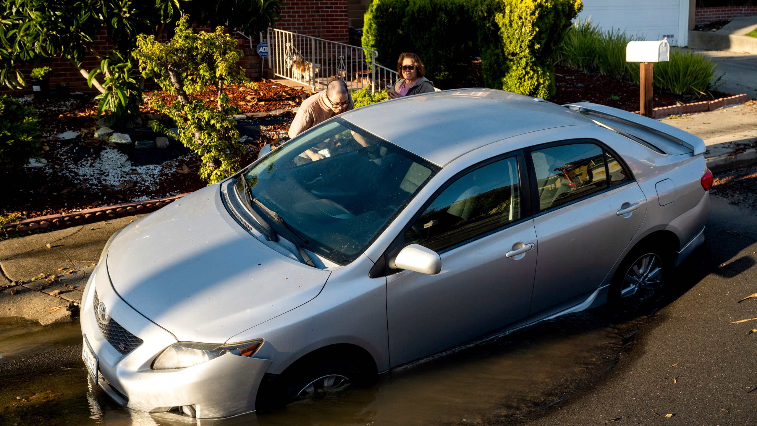 Rolo Tanedo Jr. looks inside his car, which became stuck in a sinkhole, as firefighters battle the Keller Fire burning in Oakland, Calif., Friday, Oct. 18, 2024. (AP Photo/Noah Berger)