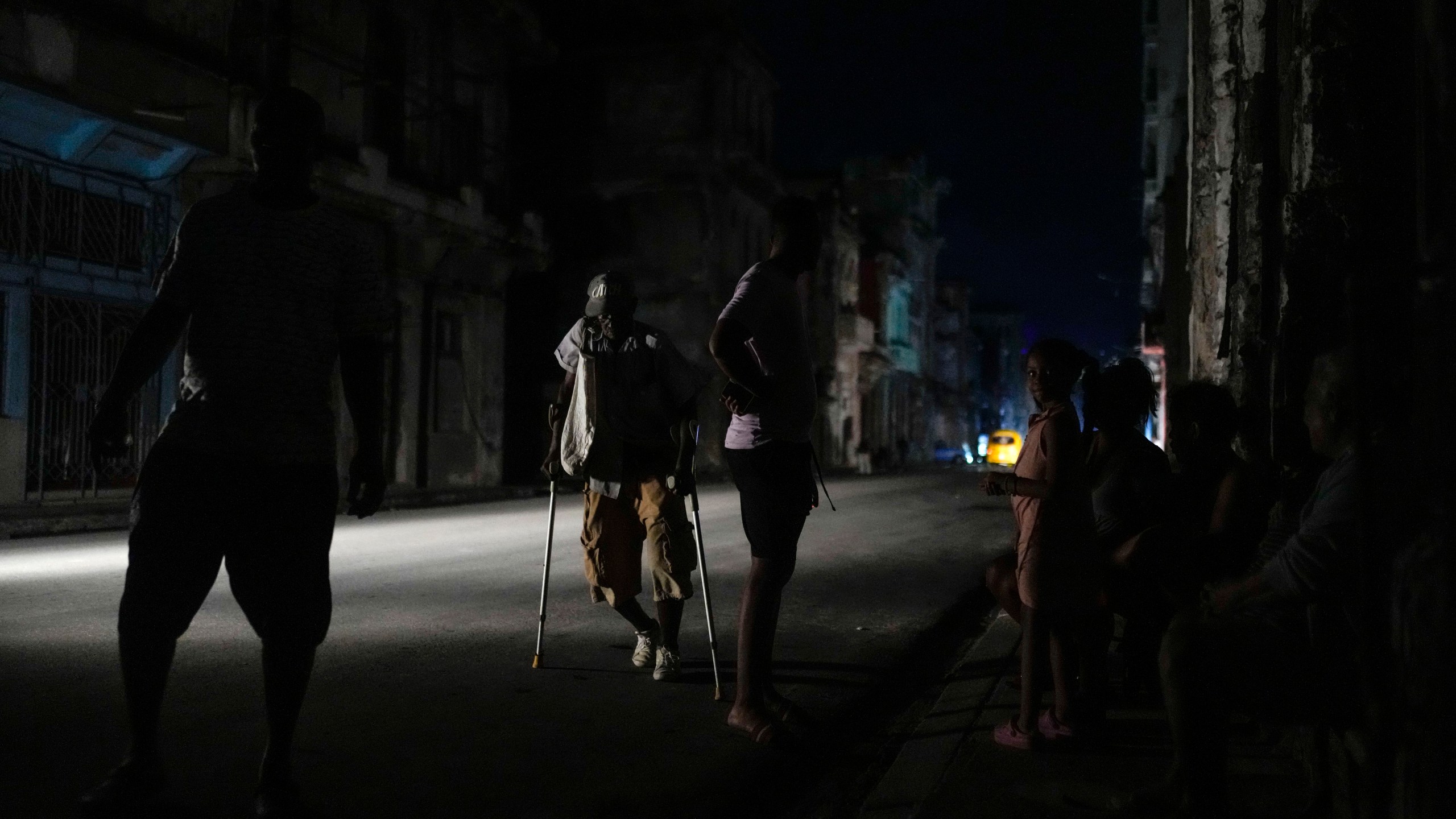 A man walks along a street with the aid of crutches during a massive blackout after a major power plant failed in Havana, Cuba, Friday, Oct. 18, 2024. (AP Photo/Ramon Espinosa)