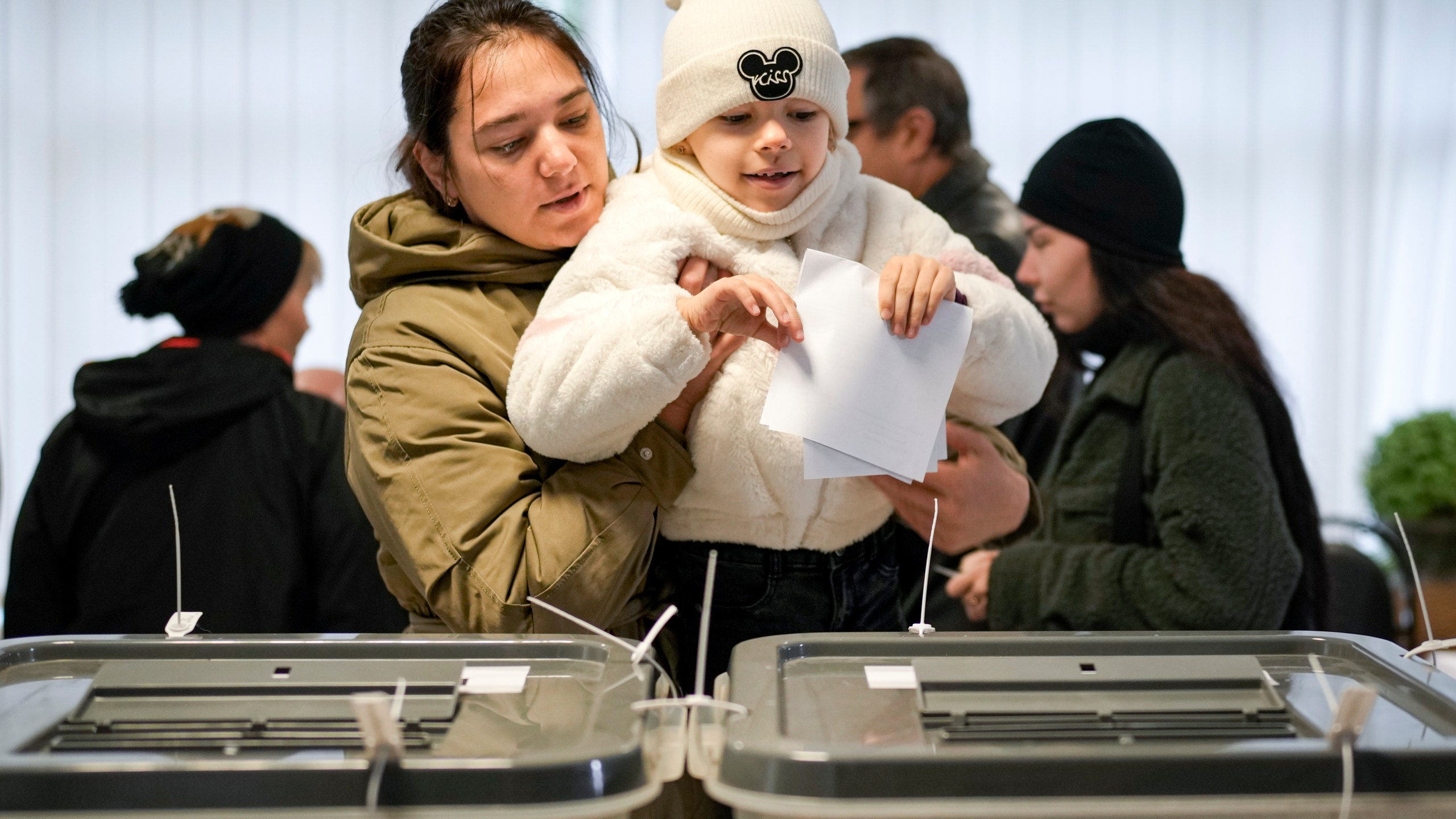 A woman holds a child as she casts her vote in Chisinau, Moldova, Sunday, Oct. 20, 2024, during a presidential election and a referendum on whether to enshrine in the Constitution the country's path to European Union membership. (AP Photo/Vadim Ghirda)