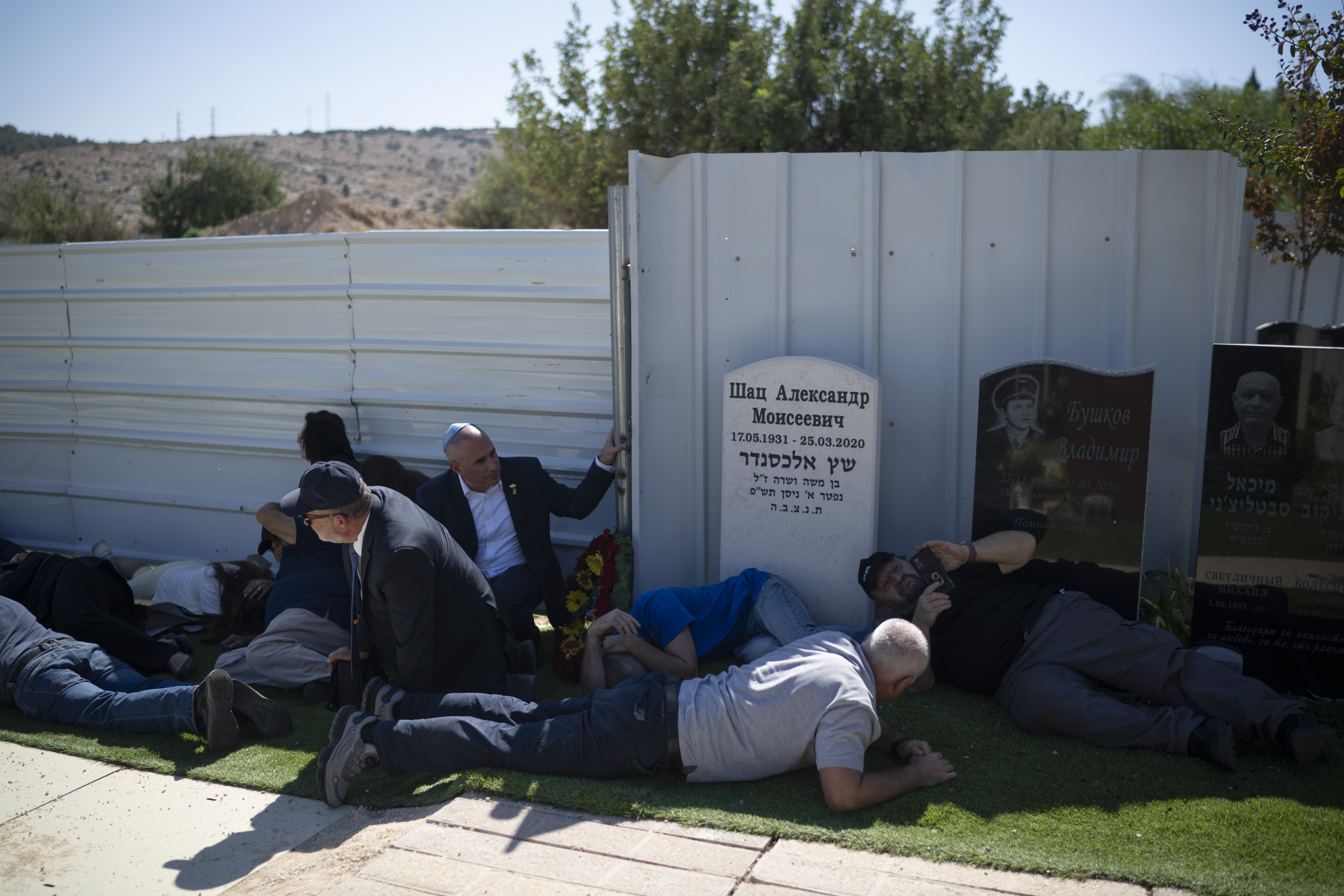 People take cover as a siren warns of incoming rockets during the funeral of Alexei Popov, who was killed during a rocket attack fired from Lebanon last weekend, at the Tel Regev cemetery in the outskirts of Haifa, northern Israel, Monday, Oct. 21, 2024. (AP Photo/Leo Correa)