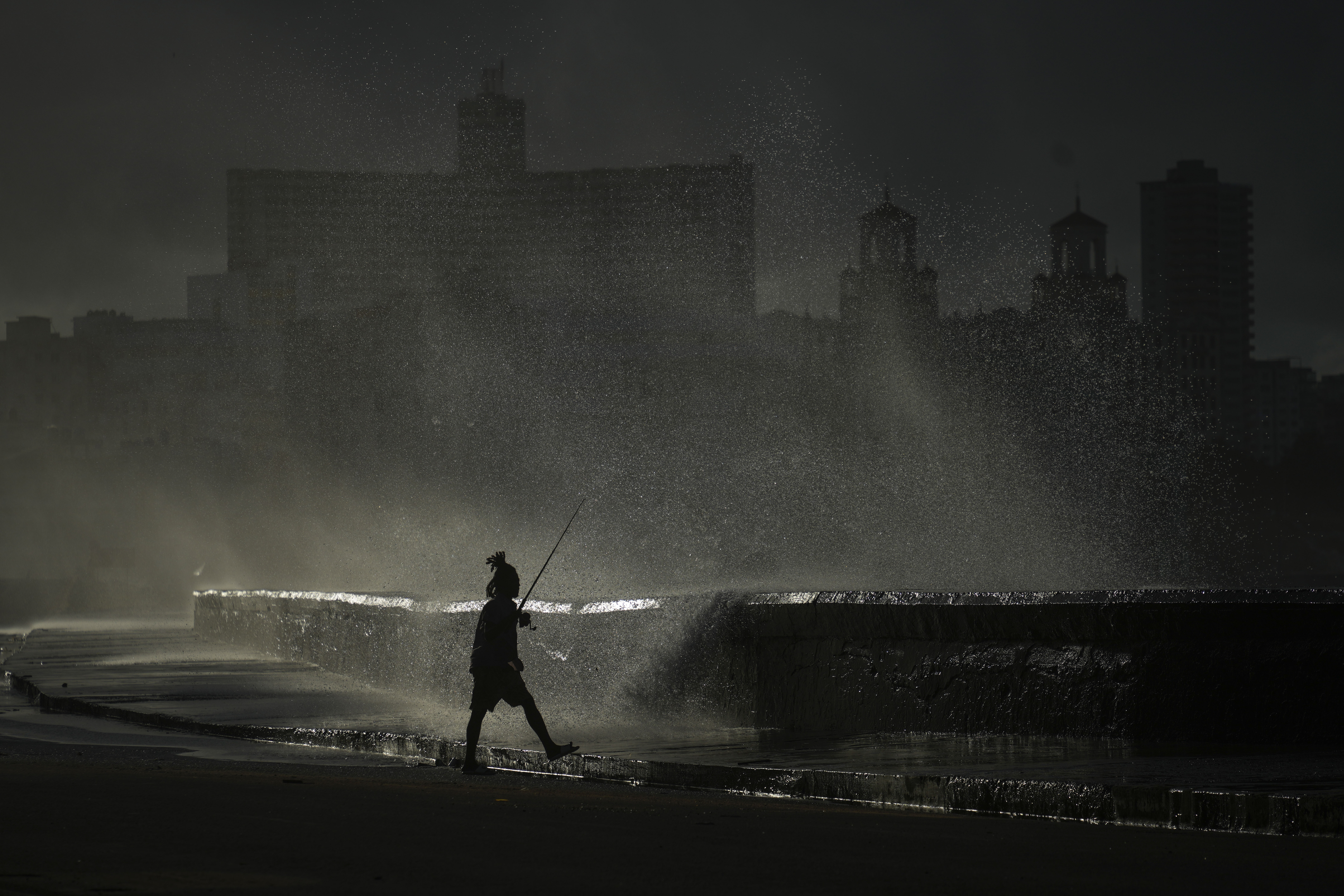 A person fishes along the boardwalk as waves crash during a power outage in Havana, Monday, Oct. 21, 2024. (AP Photo/Ramon Espinosa)