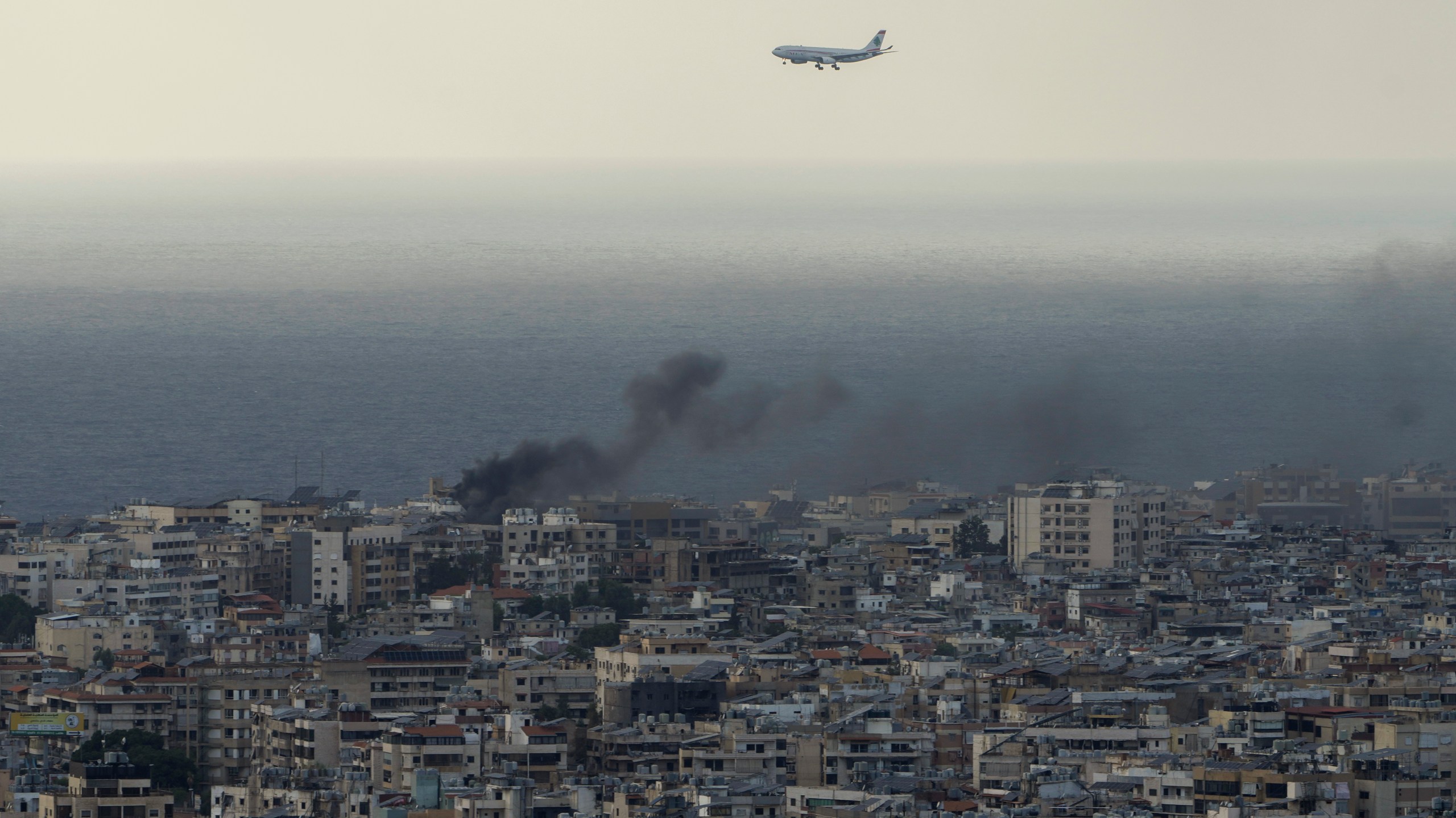 A Middle East Airlines airplane flies over Beirut as smoke rises from Israeli airstrikes in Dahiyeh, Beirut, Tuesday, Oct. 1, 2024. (AP Photo/Bilal Hussein)