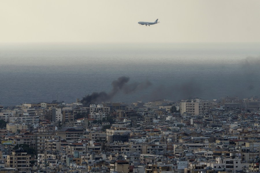 A Middle East Airlines airplane flies over Beirut as smoke rises from Israeli airstrikes in Dahiyeh, Beirut, Tuesday, Oct. 1, 2024. (AP Photo/Bilal Hussein)