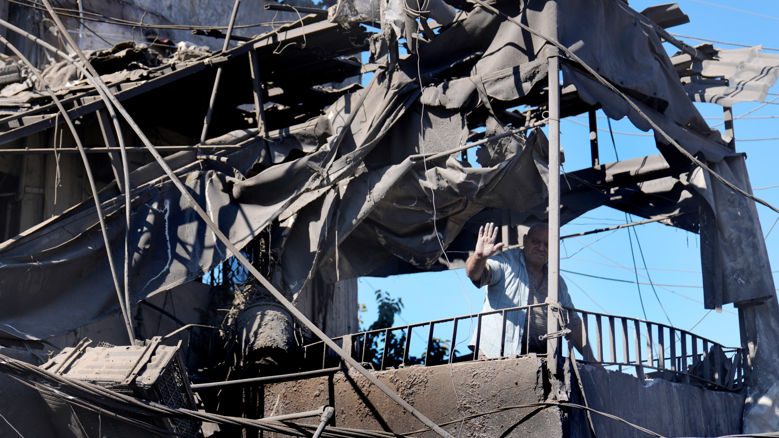 A man waves from his shattered house at the site of Israeli airstrikes that destroyed buildings facing the city's main government hospital in a densely-populated neighborhood, in southern Beirut, Lebanon, Tuesday, Oct. 22, 2024. (AP Photo/Hussein Malla)