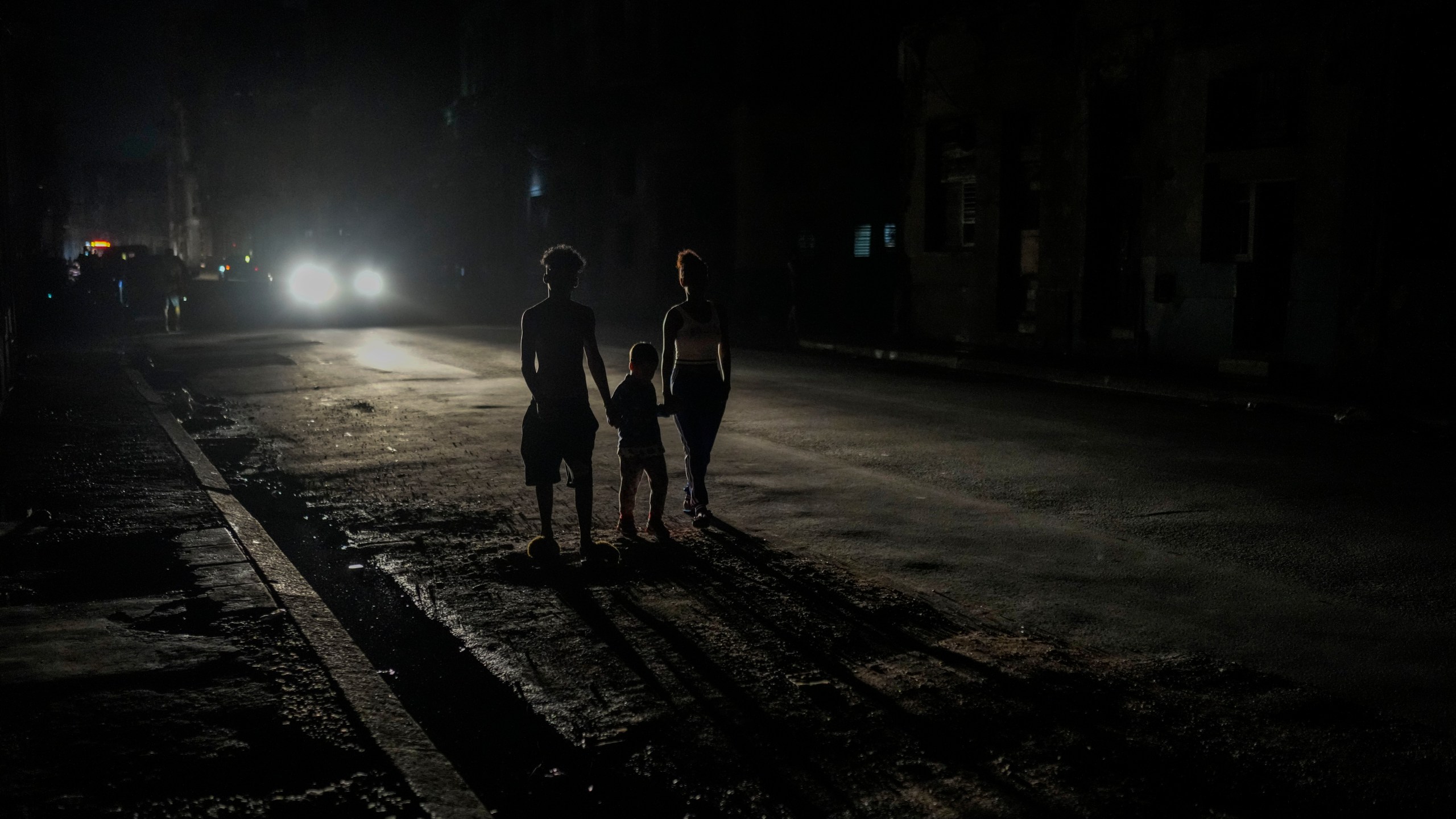 FILE - Residents are illuminated by the headlights of a car during a blackout after a major power plant failed in Havana, Cuba, Oct. 18, 2024. (AP Photo/Ramon Espinosa, File)