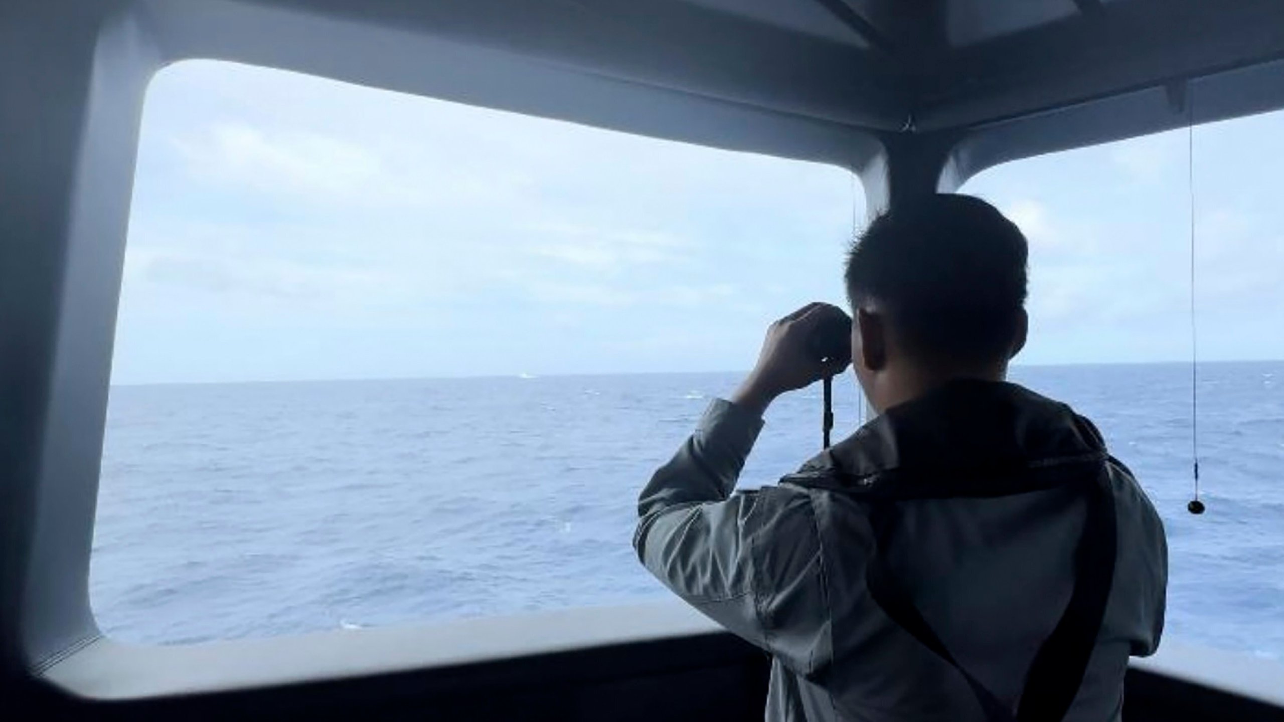 In this undated released by Indonesian Maritime Security Agency (BAKAMLA), a Maritime Security Agency uses a binocular to monitor the movement of a a Chinese coast guard vessel in the water of North Natuna Sea in the disputed area of the South China Sea, Indonesia, Thursday, Oct. 24, 2024. (BAKAMLA via AP)