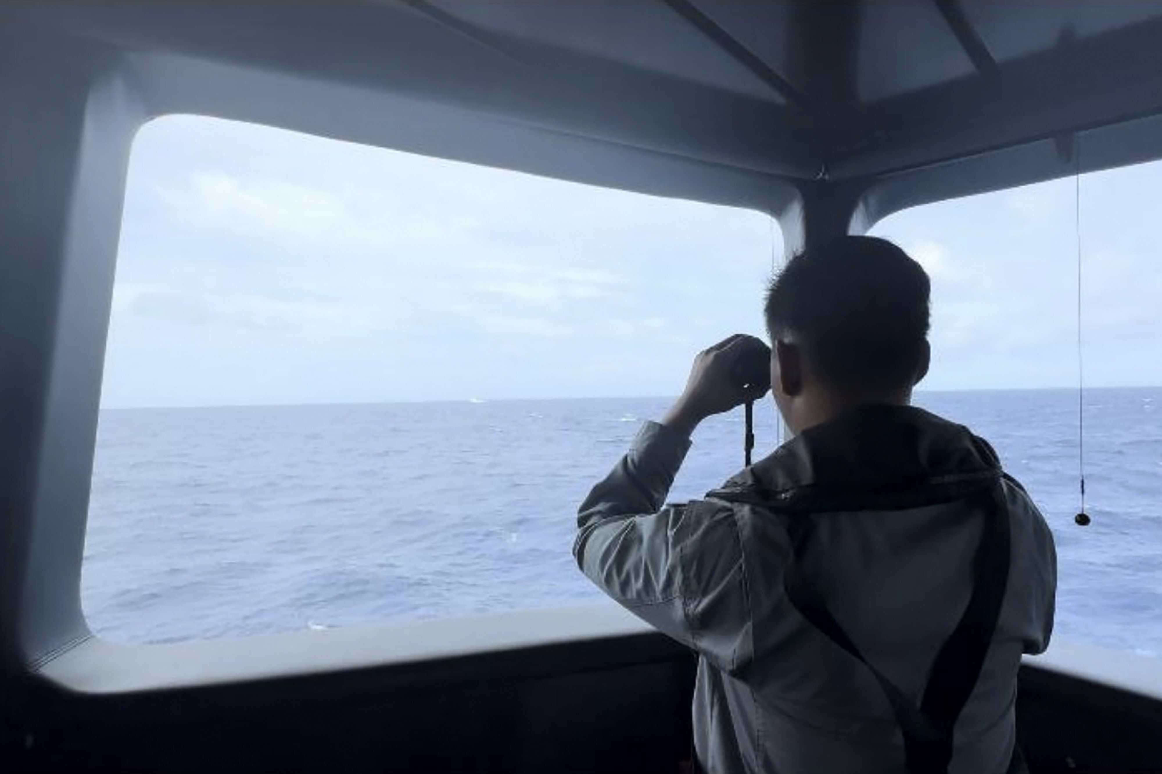 In this undated released by Indonesian Maritime Security Agency (BAKAMLA), a Maritime Security Agency uses a binocular to monitor the movement of a a Chinese coast guard vessel in the water of North Natuna Sea in the disputed area of the South China Sea, Indonesia, Thursday, Oct. 24, 2024. (BAKAMLA via AP)