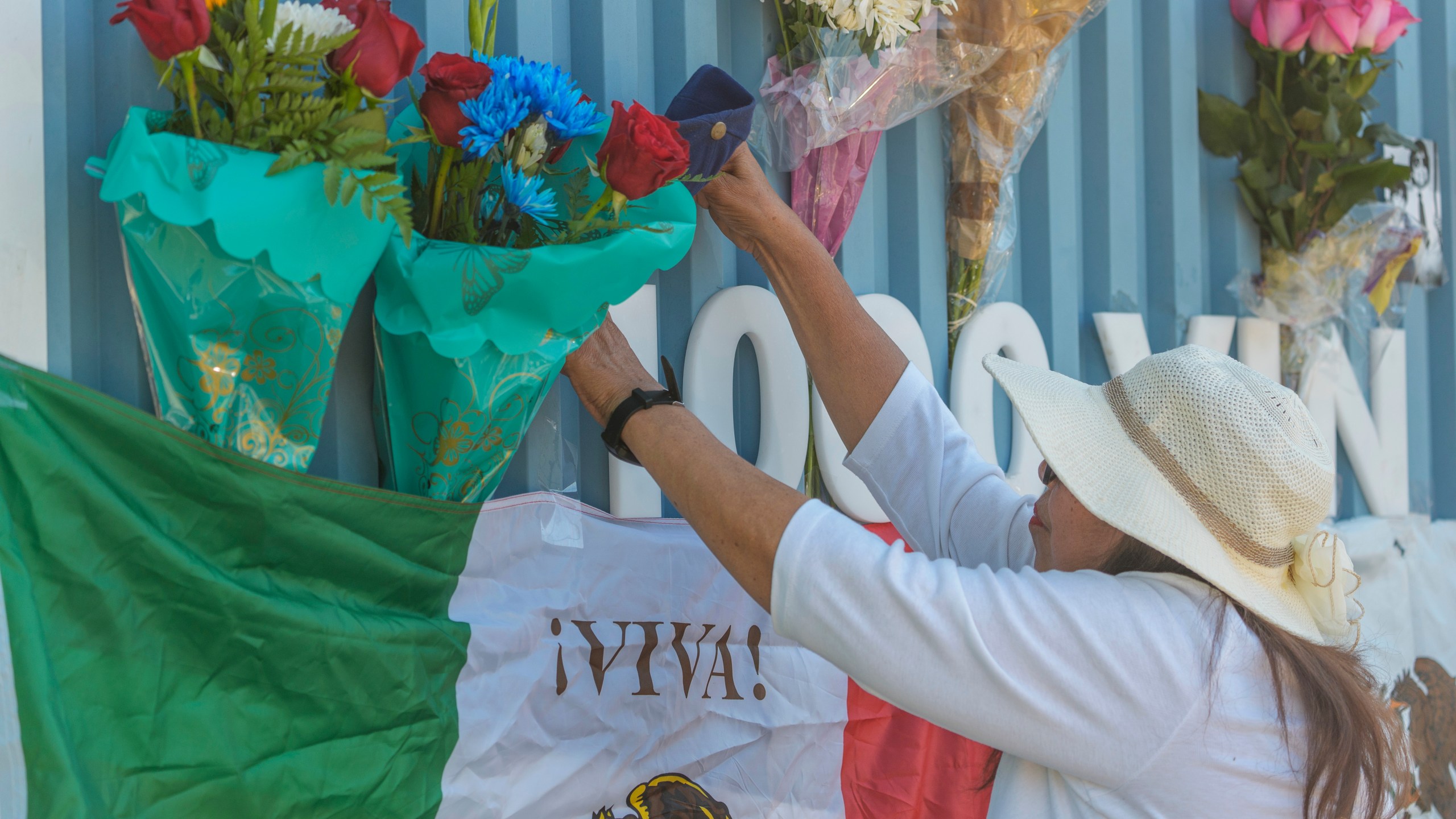 Cristina Vargas from North Hollywood, places a Mexican flag among baseball memorabilia, flowers, and candles placed outside Dodger Stadium after the death of former Dodgers pitcher Fernando Valenzuela Wednesday, Oct. 23, 2024, in Los Angeles. Valenzuela, the Mexican-born phenom for the Los Angeles Dodgers who inspired "Fernandomania" while winning the NL Cy Young Award and Rookie of the Year in 1981, died Tuesday, Oct. 22, 2024. (AP Photo/Damian Dovarganes)