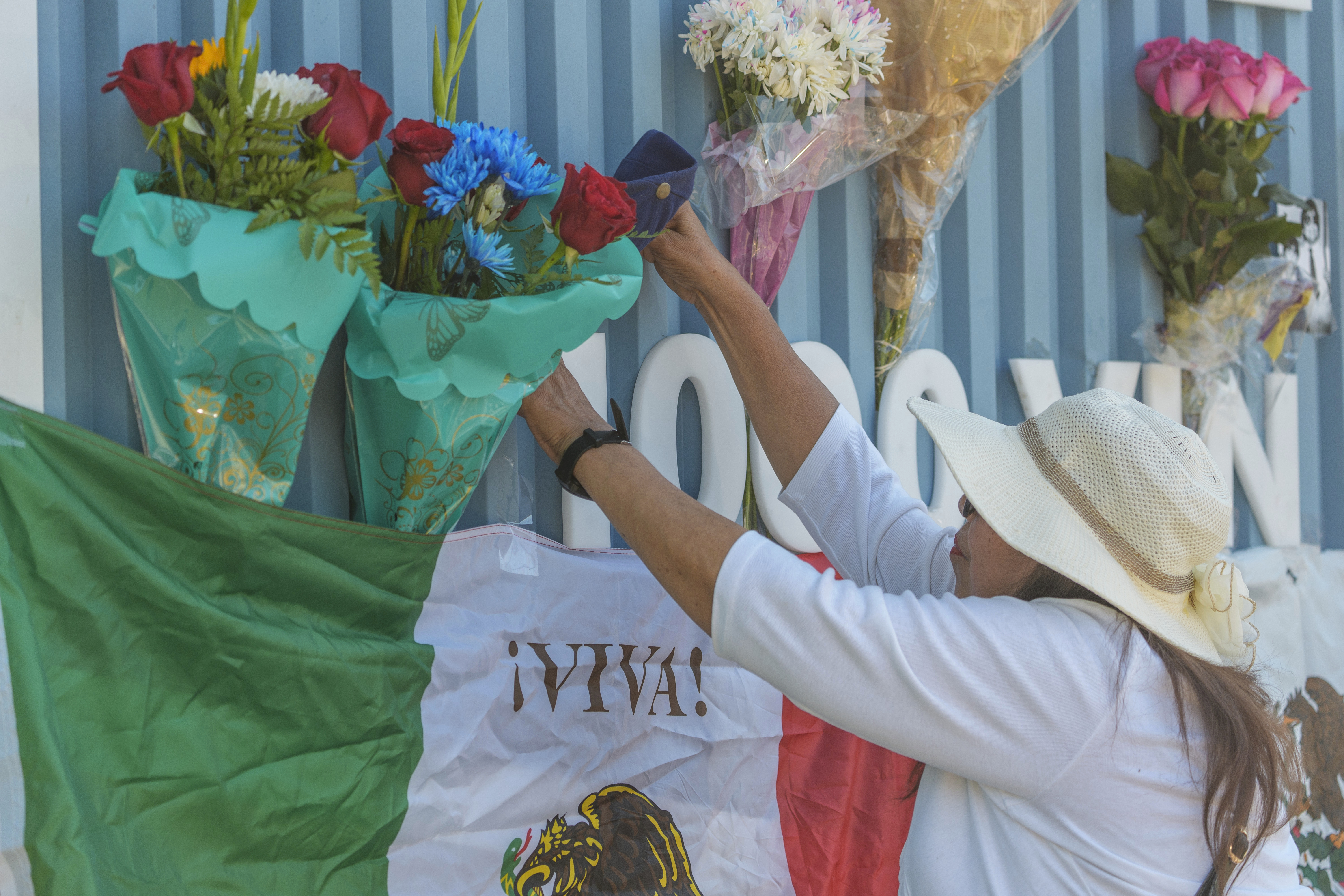 Cristina Vargas from North Hollywood, places a Mexican flag among baseball memorabilia, flowers, and candles placed outside Dodger Stadium after the death of former Dodgers pitcher Fernando Valenzuela Wednesday, Oct. 23, 2024, in Los Angeles. Valenzuela, the Mexican-born phenom for the Los Angeles Dodgers who inspired "Fernandomania" while winning the NL Cy Young Award and Rookie of the Year in 1981, died Tuesday, Oct. 22, 2024. (AP Photo/Damian Dovarganes)