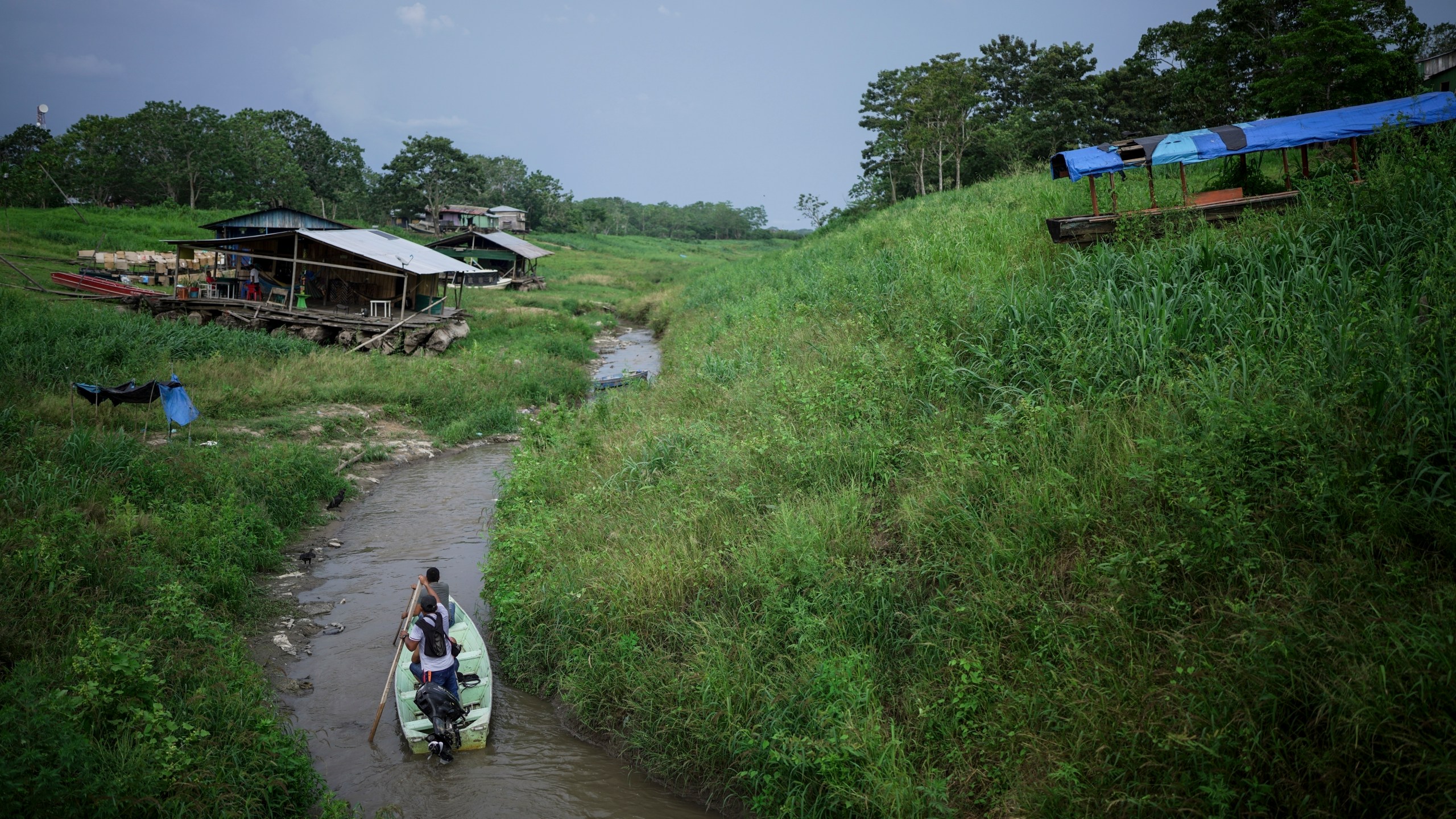 People maneuver by boat through the low level of a tributary that connects with the Amazon River, in Isla de la Fantasia, on the outskirts of Leticia, Colombia, Sunday, Oct. 20, 2024. (AP Photo/Ivan Valencia)