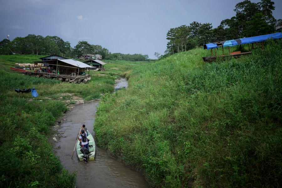 People maneuver by boat through the low level of a tributary that connects with the Amazon River, in Isla de la Fantasia, on the outskirts of Leticia, Colombia, Sunday, Oct. 20, 2024. (AP Photo/Ivan Valencia)