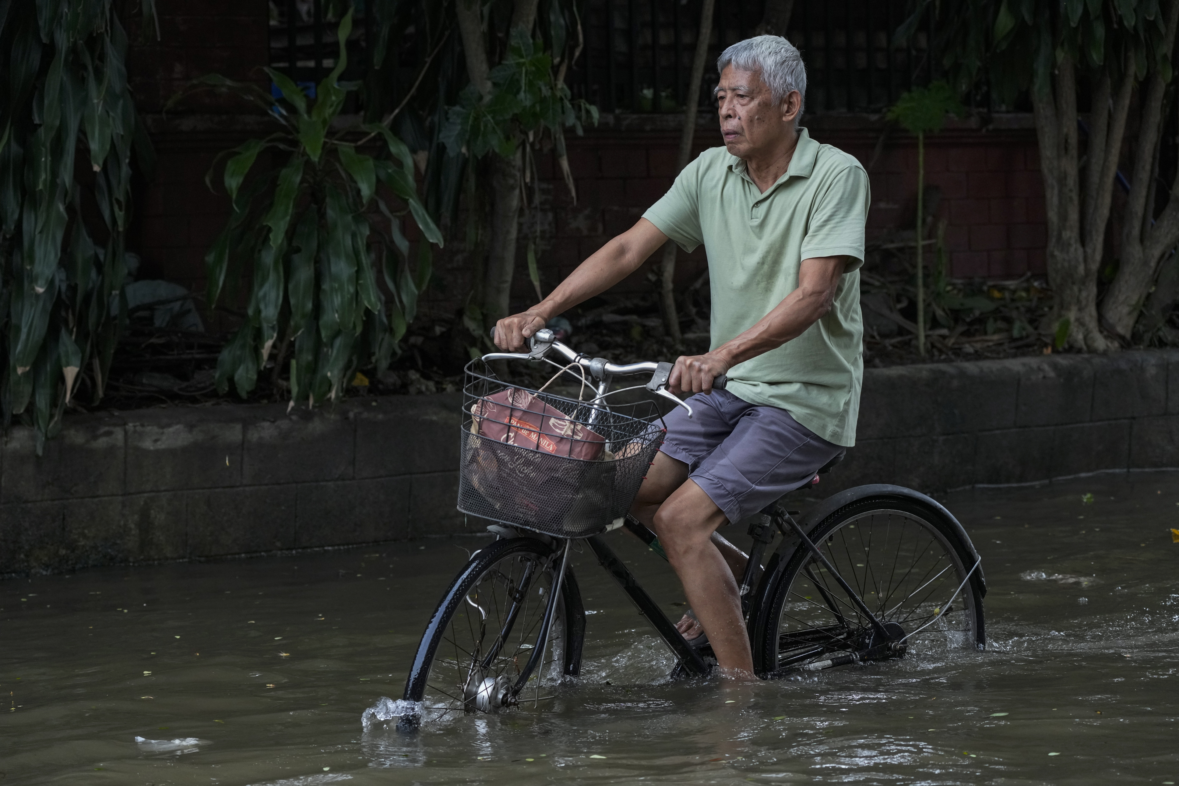 A resident rides his bike as he crosses flooded streets caused by Tropical Storm Trami on Friday, Oct. 25, 2024, in Cainta, Rizal province, Philippines. (AP Photo/Aaron Favila)