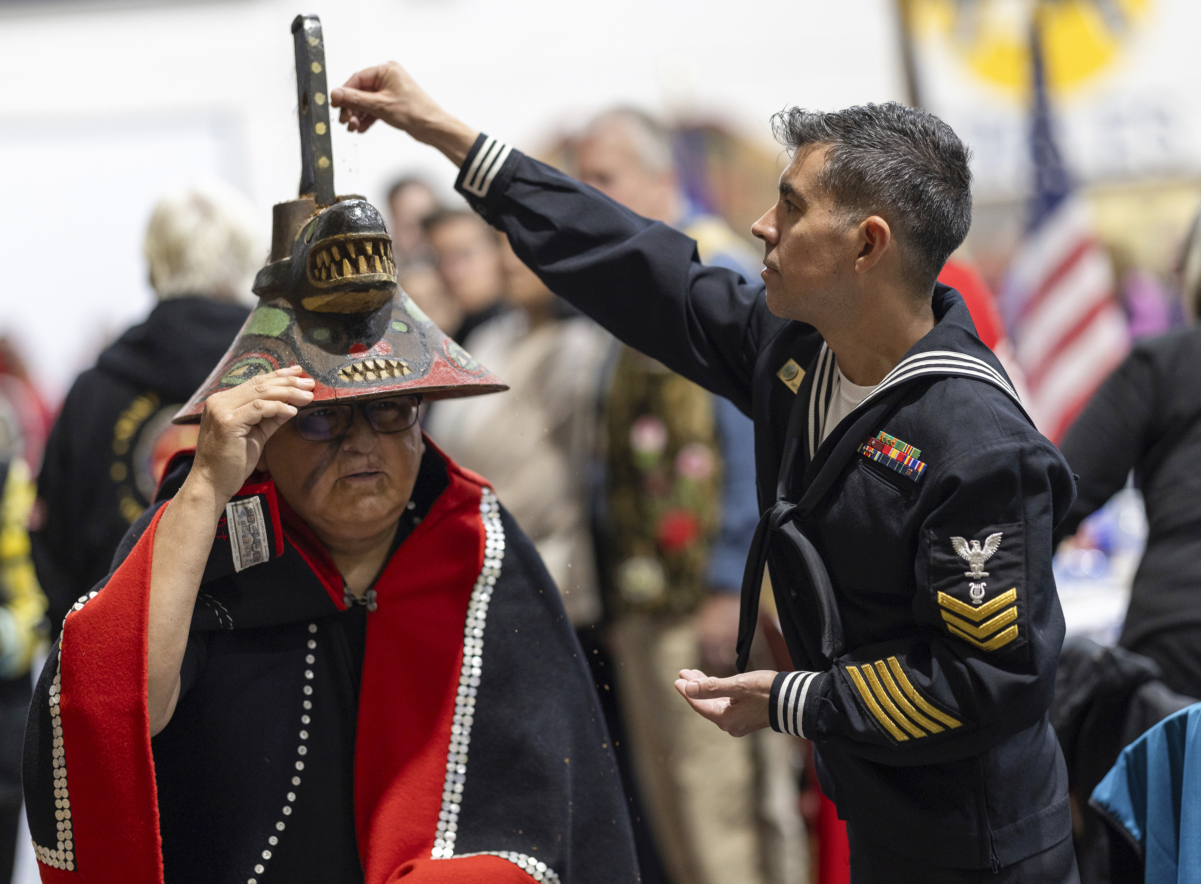 A member of the U.S. Navy sprinkles tobacco on top of a killer whale clan hat, which is considered to bring good fortune, during a Navy ceremony Saturday, Oct. 26, 2024, in Angoon, Alaska, to apologize for the 1882 military bombing of the Tlingit village in Angoon. (Nobu Koch/Sealaska Heritage Institute via AP)