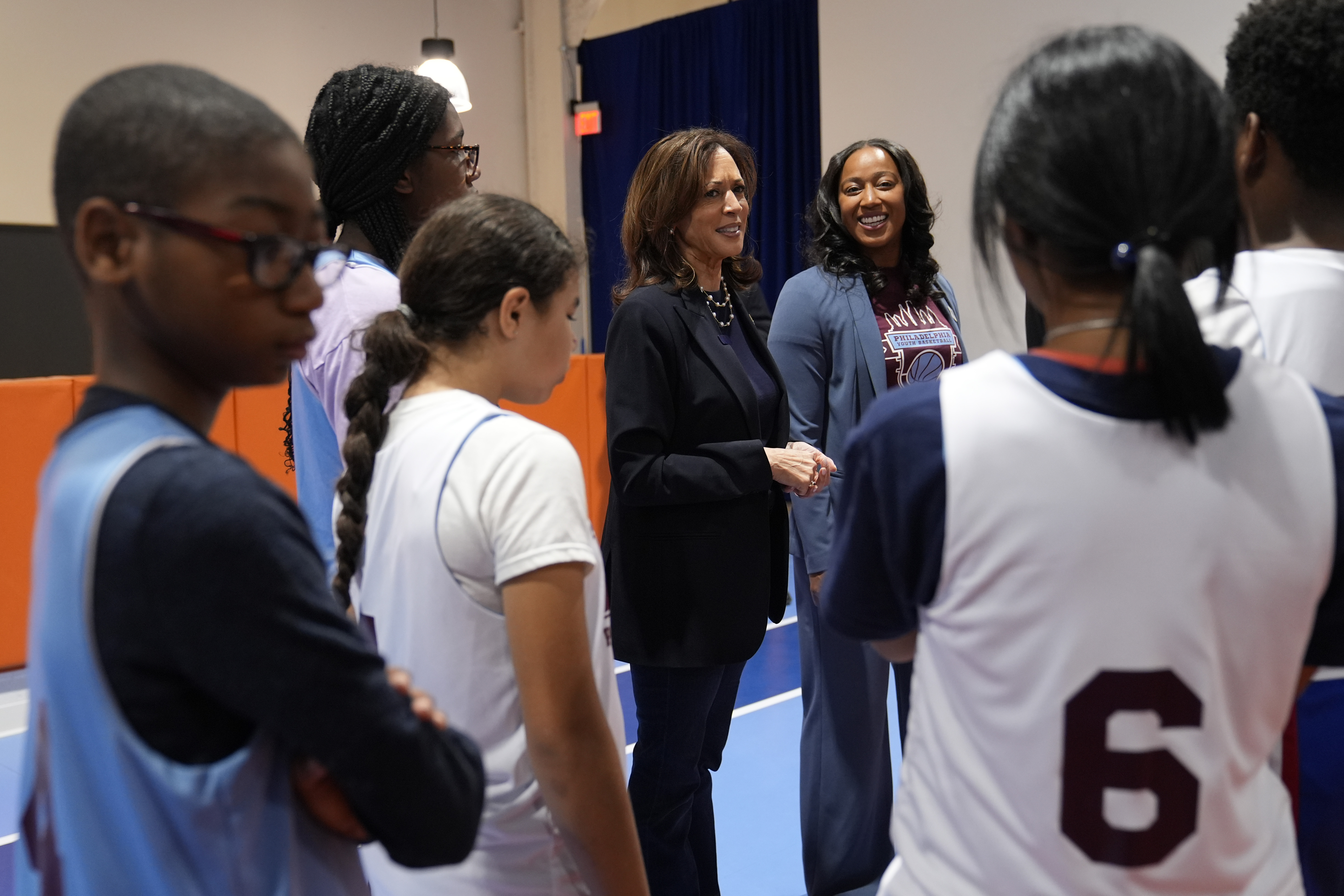 Democratic presidential nominee Vice President Kamala Harris, center, speaks with young basketball players alongide coach Randyll Butler, right, before a community rally at the Alan Horwitz "Sixth Man" Center, Sunday, Oct. 27, 2024, in Philadelphia. (AP Photo/Susan Walsh)