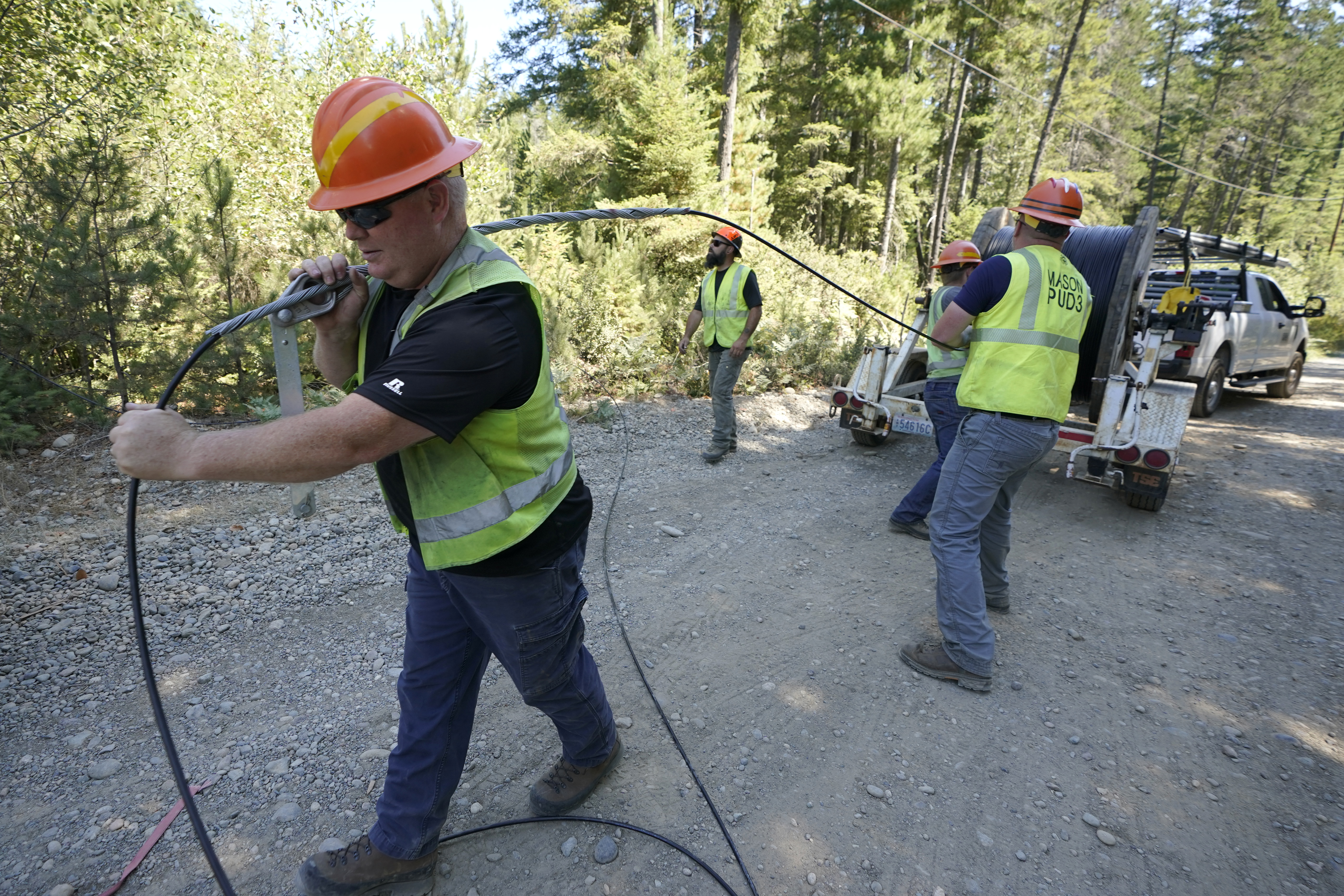 FILE - Carl Roath, left, a worker with the Mason County (Wash.) Public Utility District, pulls fiber optic cable on a project to install broadband internet service in the area surrounding Lake Christine near Belfair, Wash., on Aug. 4, 2021. (AP Photo/Ted S. Warren, File)