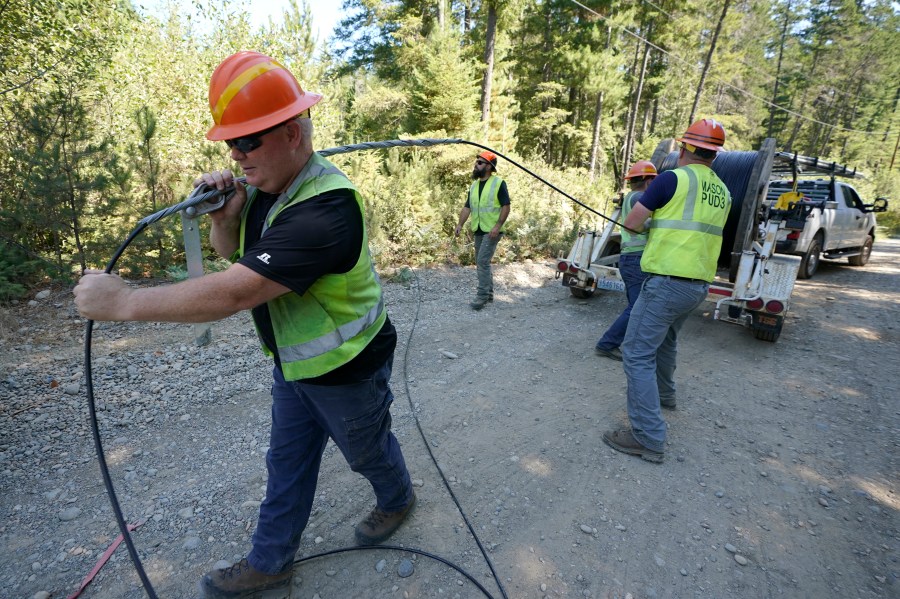 FILE - Carl Roath, left, a worker with the Mason County (Wash.) Public Utility District, pulls fiber optic cable on a project to install broadband internet service in the area surrounding Lake Christine near Belfair, Wash., on Aug. 4, 2021. (AP Photo/Ted S. Warren, File)