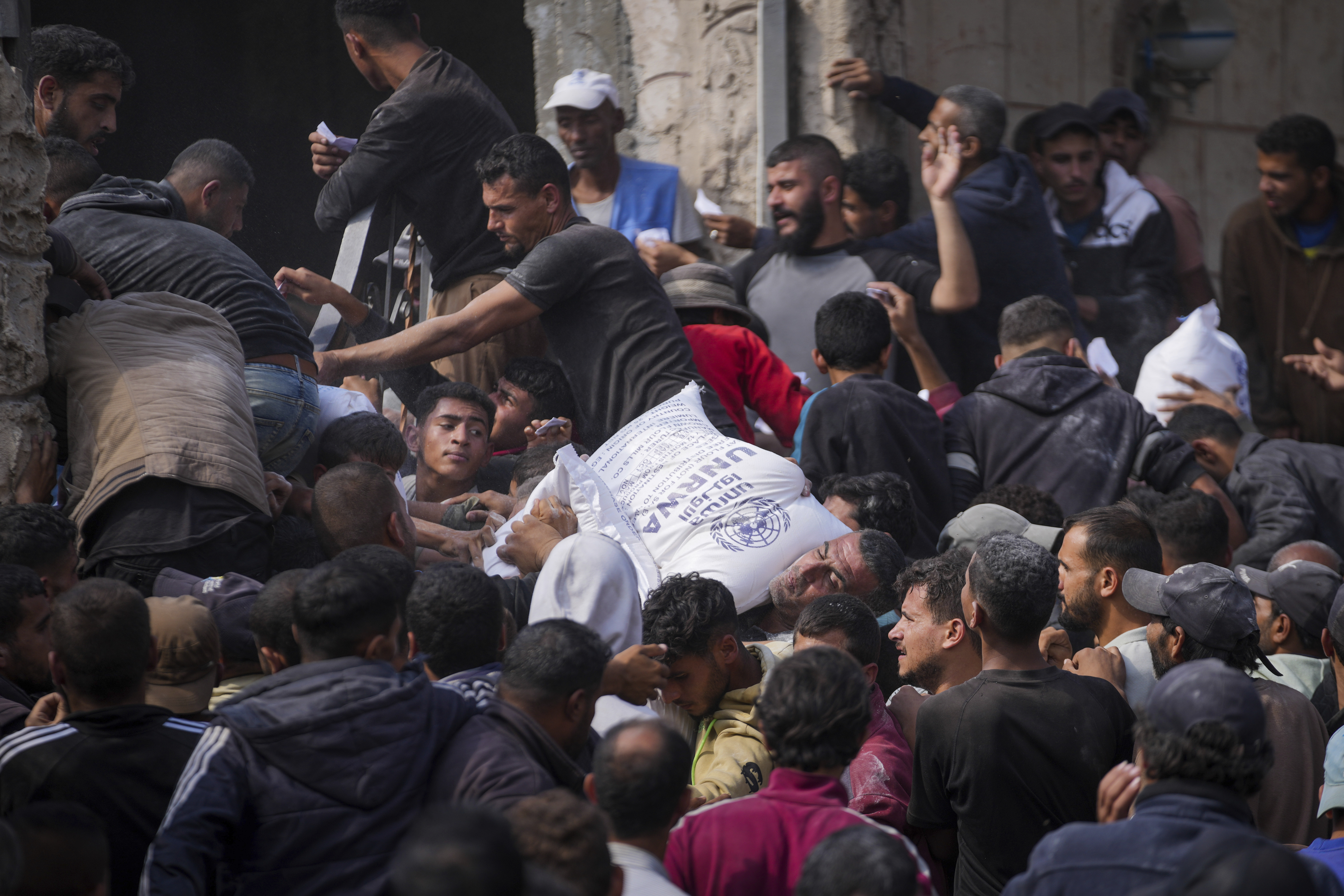 Palestinians gather to receive bags of flour distributed by UNRWA, the U.N. agency helping Palestinian refugees, in Deir al Balah, central Gaza Strip, Saturday, Nov. 2, 2024. (AP Photo/Abdel Kareem Hana)