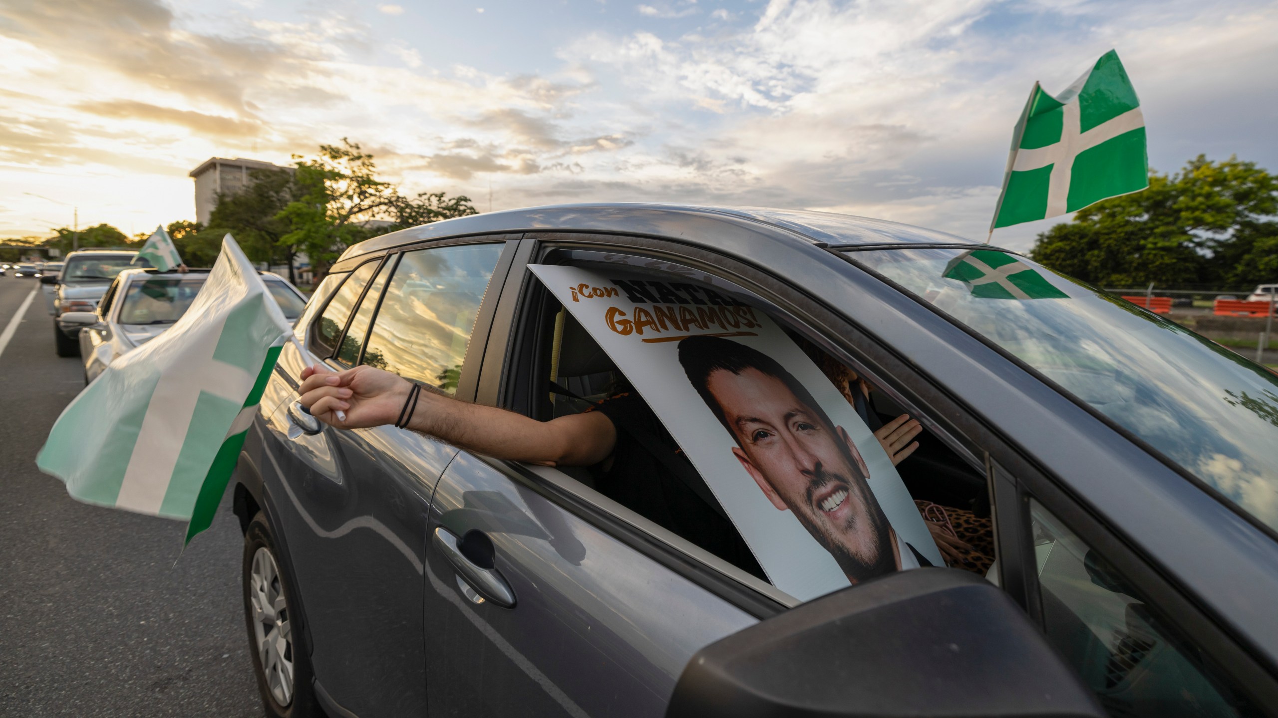 A supporter waves a Puerto Rican Independence Party flag while holding a campaign poster promoting the Citizens' Victory Movement mayoral candidate Manuel Natal, during a caravan in San Juan, Puerto Rico, Friday, Nov. 1, 2024. (AP Photo/Alejandro Granadillo)