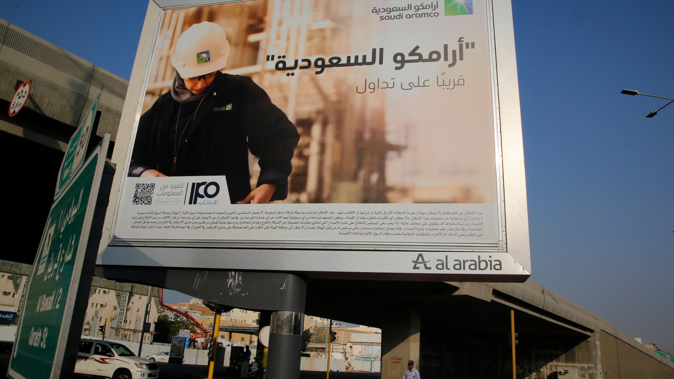 FILE - A man walks under a billboard displaying an advertisement for Saudi Arabia's state-owned oil giant Aramco with Arabic reading "Saudi Aramco, soon on stock exchange" in Jiddah, Saudi Arabia, on Nov. 12, 2019. (AP Photo/Amr Nabil, File)