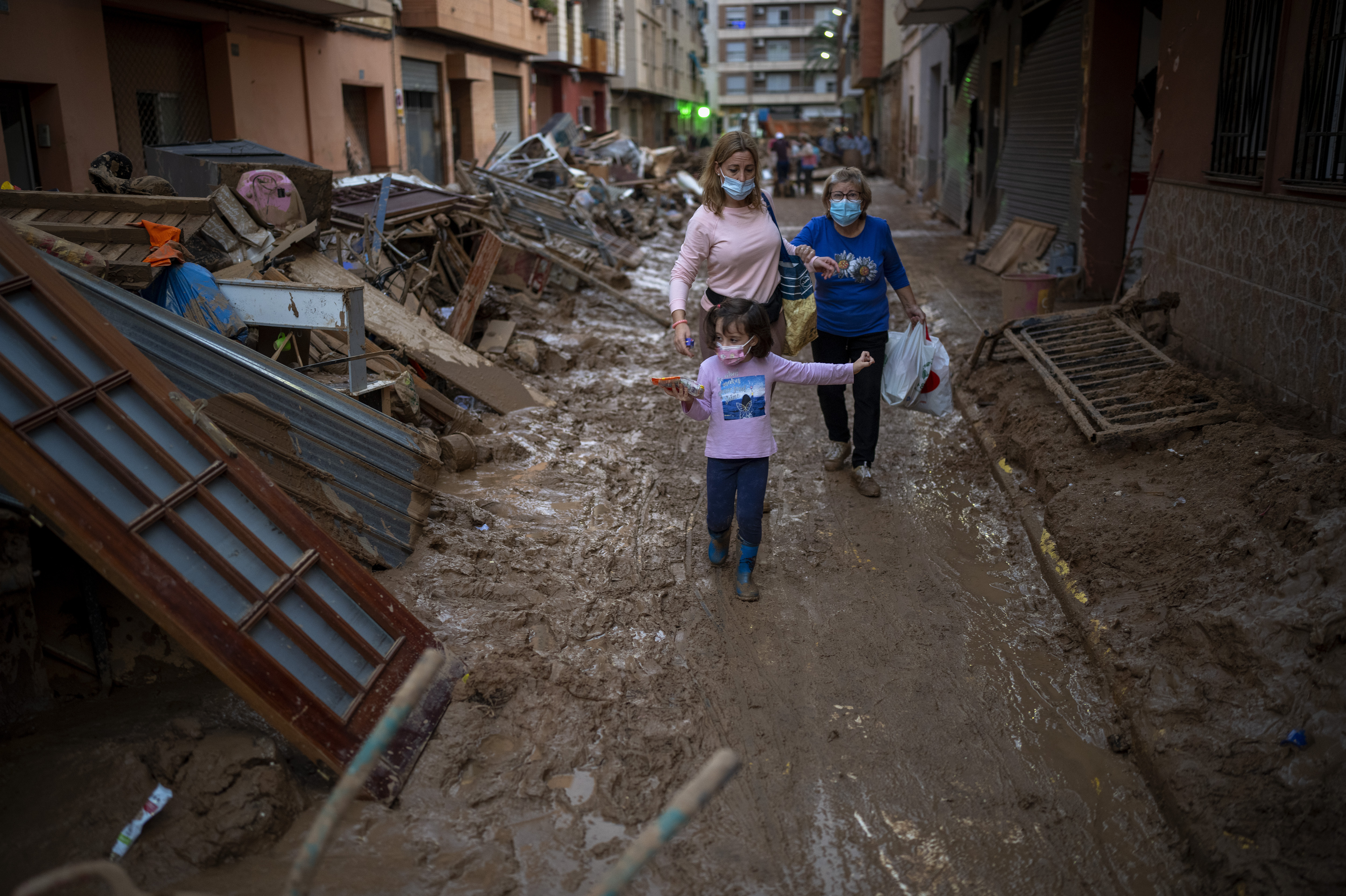 A child walks with her mother and grandmother through a street with piled furniture and rubbish on the sides, in an area affected by floods in Paiporta, Valencia, Spain, Tuesday, Nov. 5, 2024. (AP Photo/Emilio Morenatti)