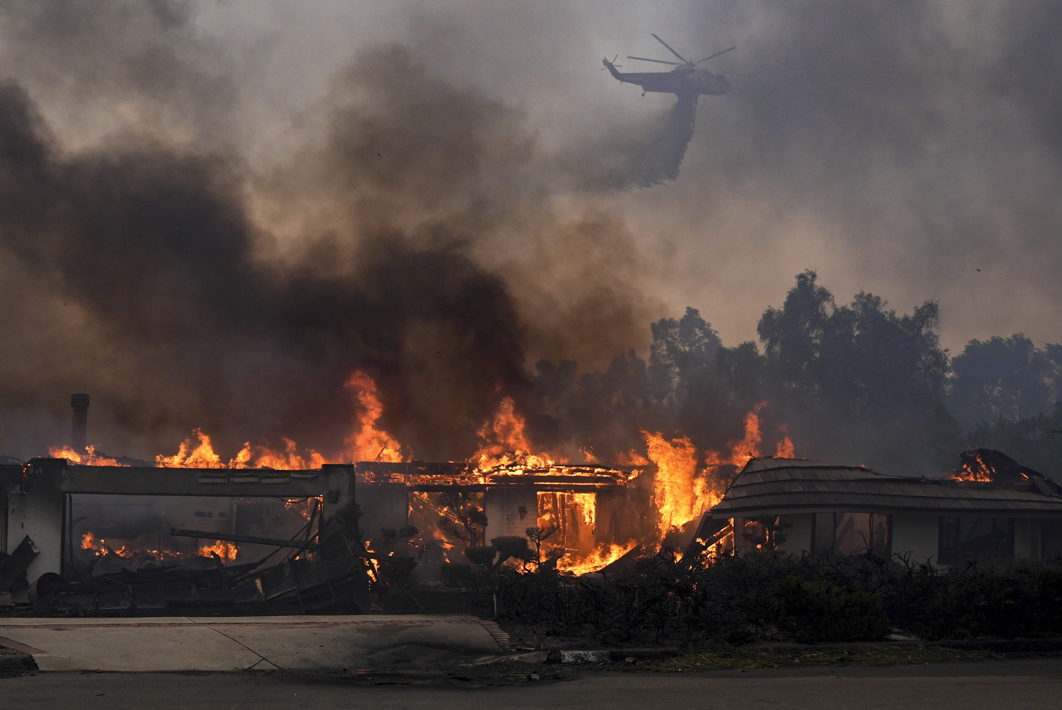 A helicopter drops water over a burning home in the Mountain fire, Wednesday, Nov. 6, 2024, near Camarillo, Calif. (AP Photo/Marcio Jose Sanchez)