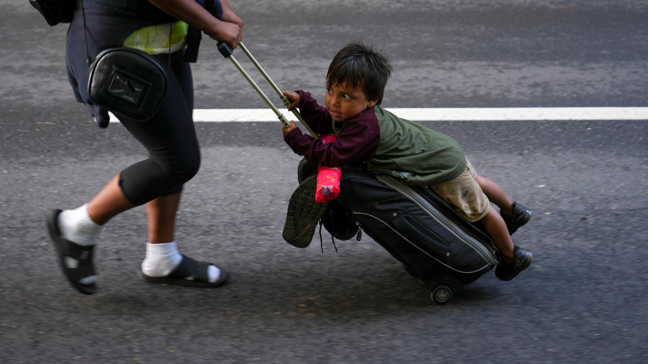 Nayely Nunez, from Honduras, uses her luggage to carry a child as she walks along the highway with a migrant caravan in Huixtla, southern Mexico, heading toward the country's northern border and ultimately the United States, Thursday, Nov. 7, 2024. (AP Photo/Moises Castillo)