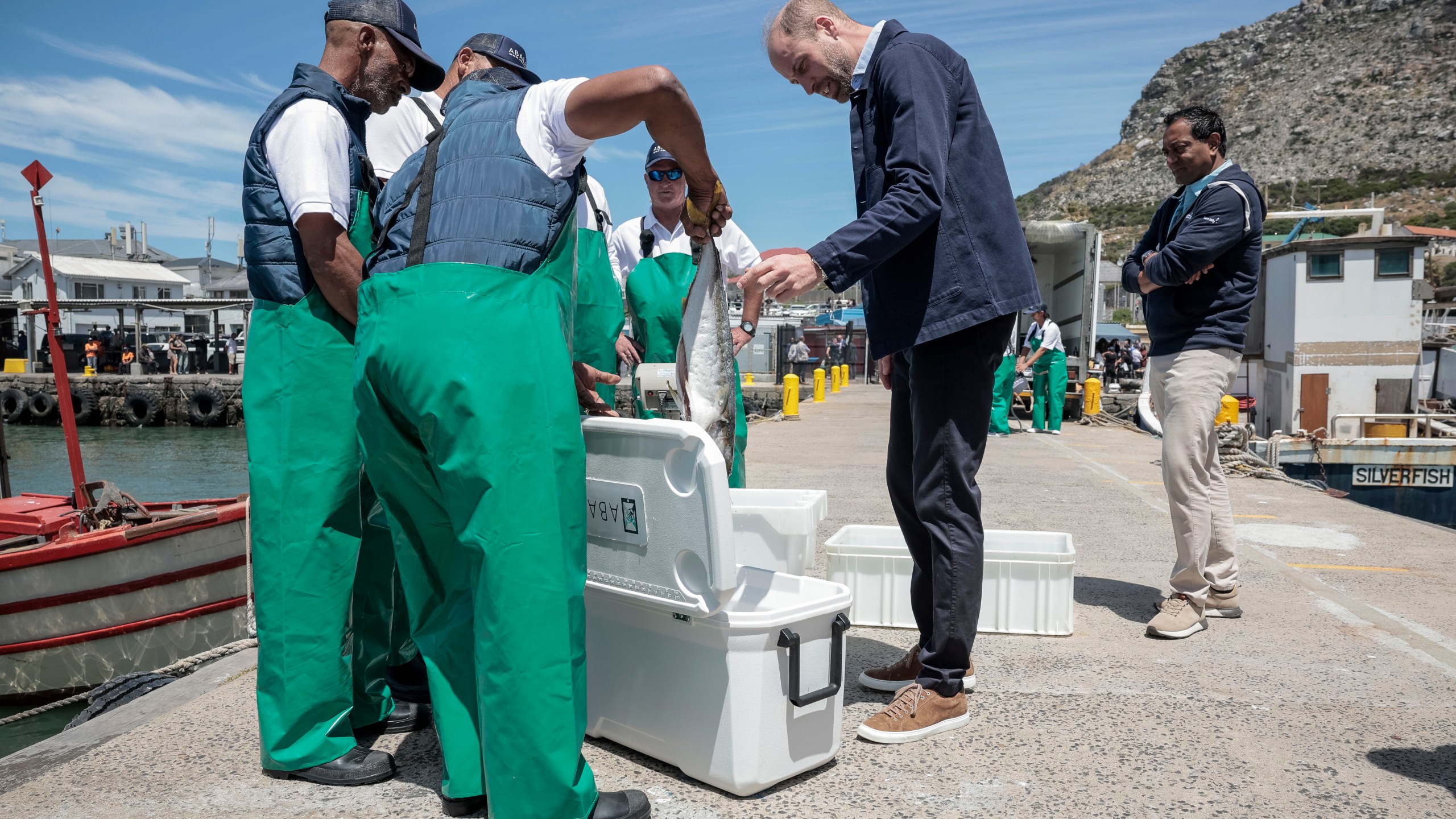 Britain's Prince William, the Prince of Wales is handed a fish as he speaks to local fisherman, at Kalk Bay Harbour, near Cape Town, Thursday, Nov. 7, 2024. (Gianluigi Guercia/Pool Photo via AP)