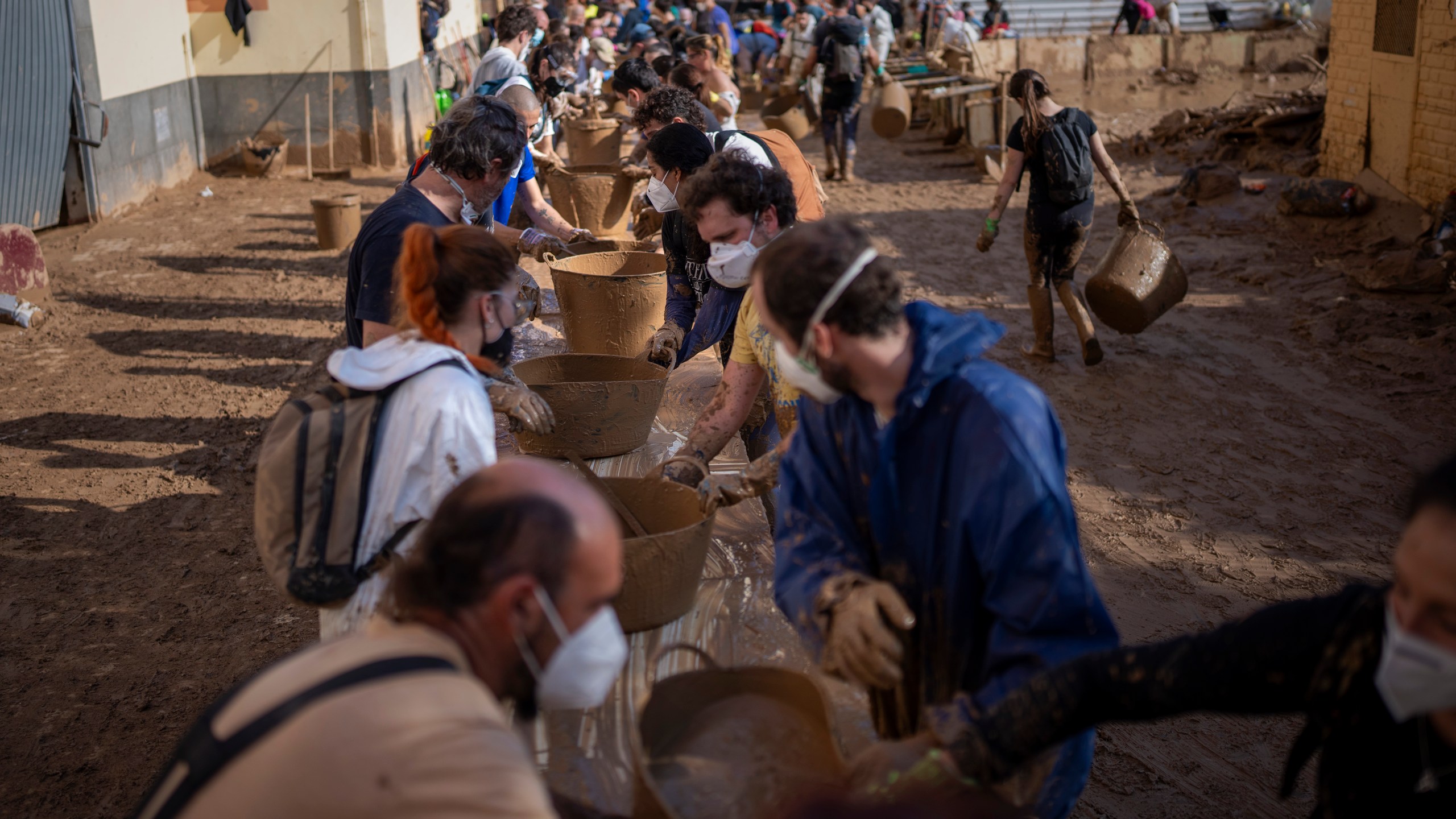 Volunteers make a human chain to evacuate the mud in buckets in an area still flooded with mud in Masanasa, Valencia, Spain, Thursday, Nov. 7, 2024. (AP Photo/Emilio Morenatti)