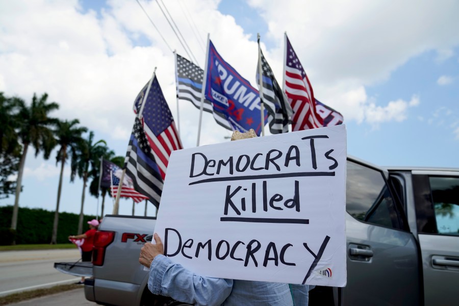 FILE - A supporter of former President Donald Trump holds a sign outside Trump International Golf Club, April 2, 2023, in West Palm Beach, Fla. (AP Photo/Evan Vucci, File)