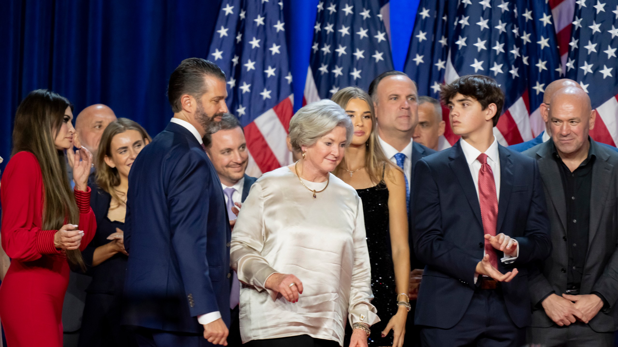 From left, Kimberly Guilfoyle, Tony Fabriozio, Donald Trump Jr., fourth from left, Justin Caporale, Susie Wiles, Kai Madison Trump, Dan Scavino, Corey Lewandowski, Donald Trump III and Dana White listen as Republican presidential nominee former President Donald Trump speaks at an election night watch party Wednesday, Nov. 6, 2024, in West Palm Beach, Fla. (AP Photo/Alex Brandon)