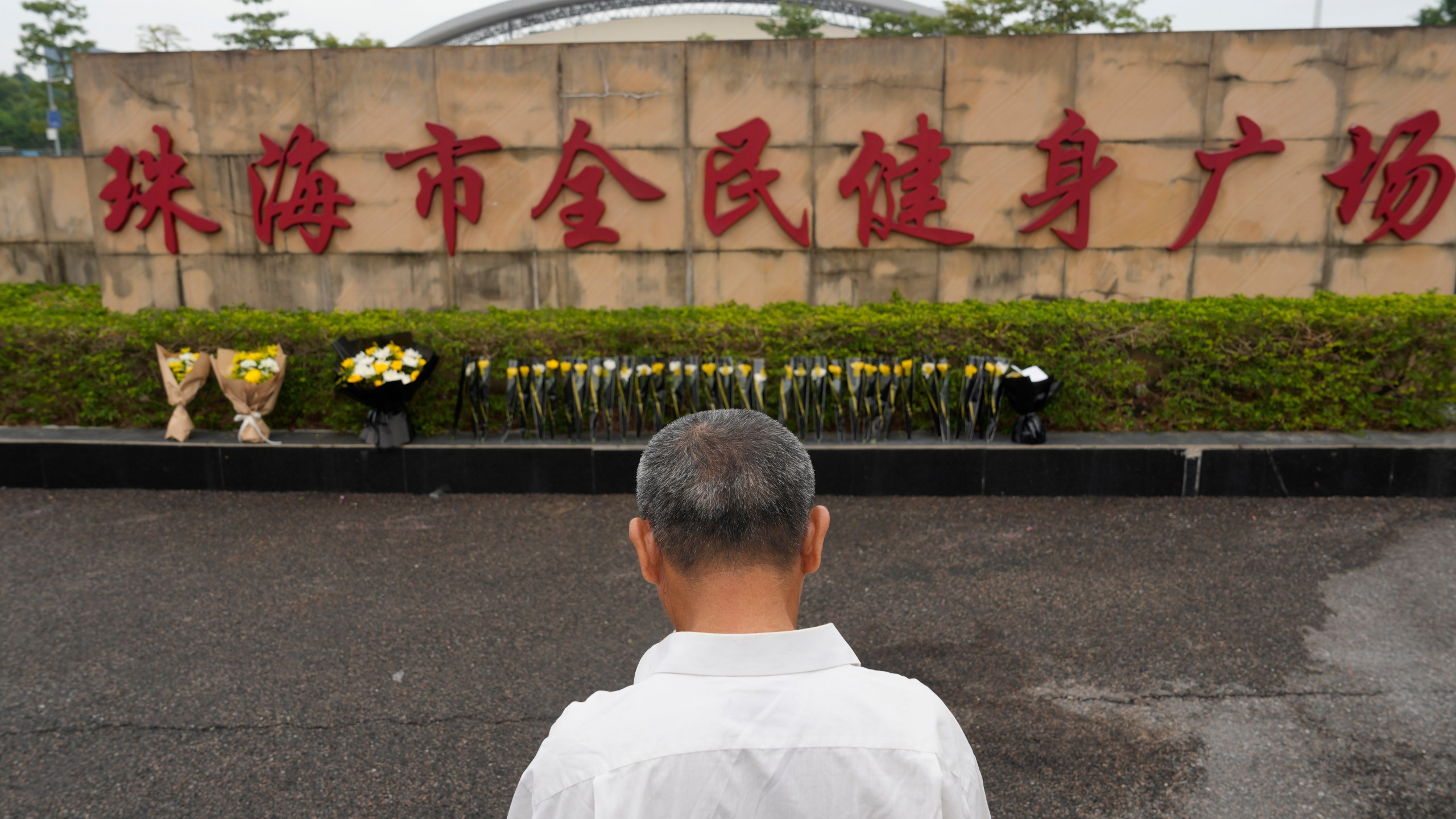 A man stands near flowers laid outside the "Zhuhai People's Fitness Plaza" where a man rammed his car into people exercising at the sports center, in Zhuhai in southern China's Guangdong province on Wednesday, Nov. 13, 2024. (AP Photo/Ng Han Guan)