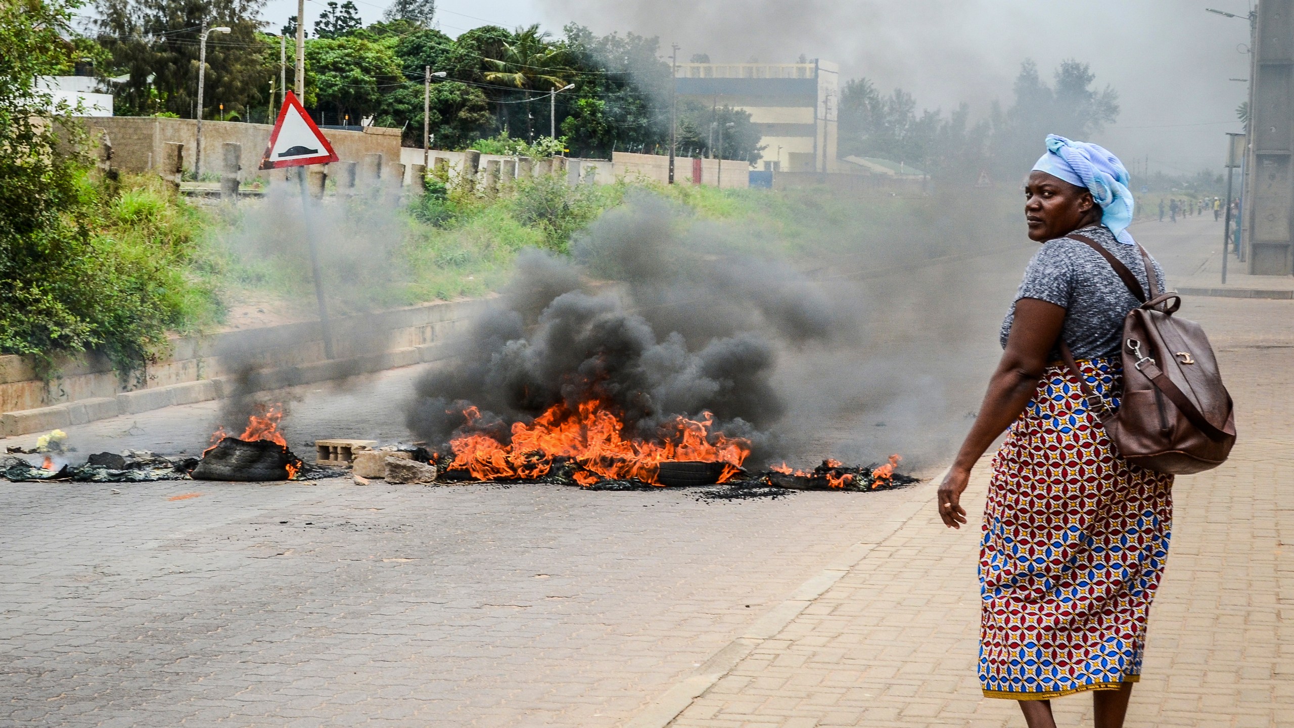 A woman walks past a barricade set fire by protesters in Maputo, Mozambique, Thursday, Nov. 7, 2024. Protesters dispute the outcome of the Oct. 9 elections that saw the ruling Frelimo party extend its 49-year rule. (AP Photo/Carlos Uqueio)