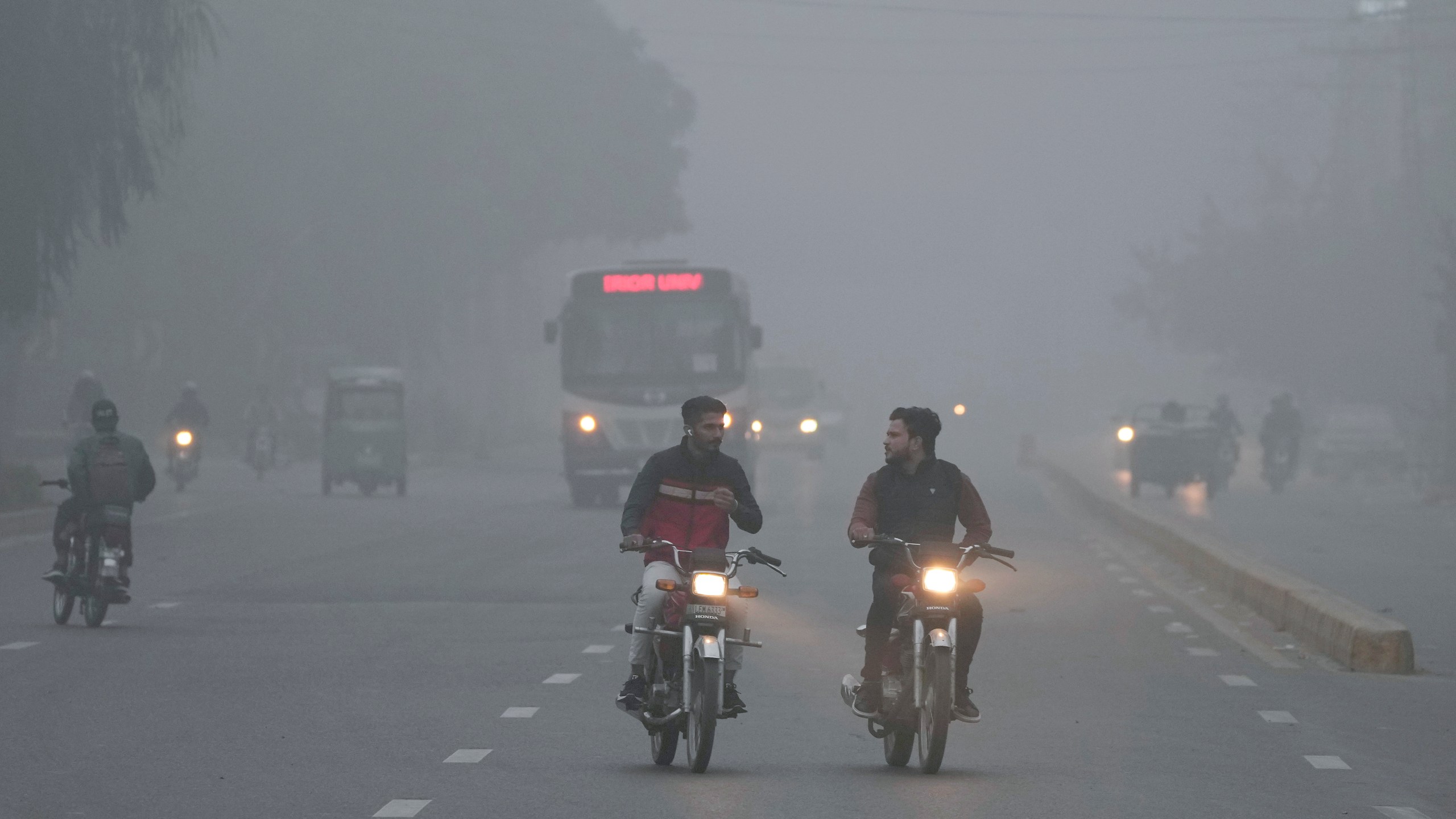 Vehicles and motorcyclists move with headlights on due to reduced visibility caused by smog enveloping the area of Lahore, Pakistan, Wednesday, Nov. 13, 2024. (AP Photo/K.M. Chaudary)