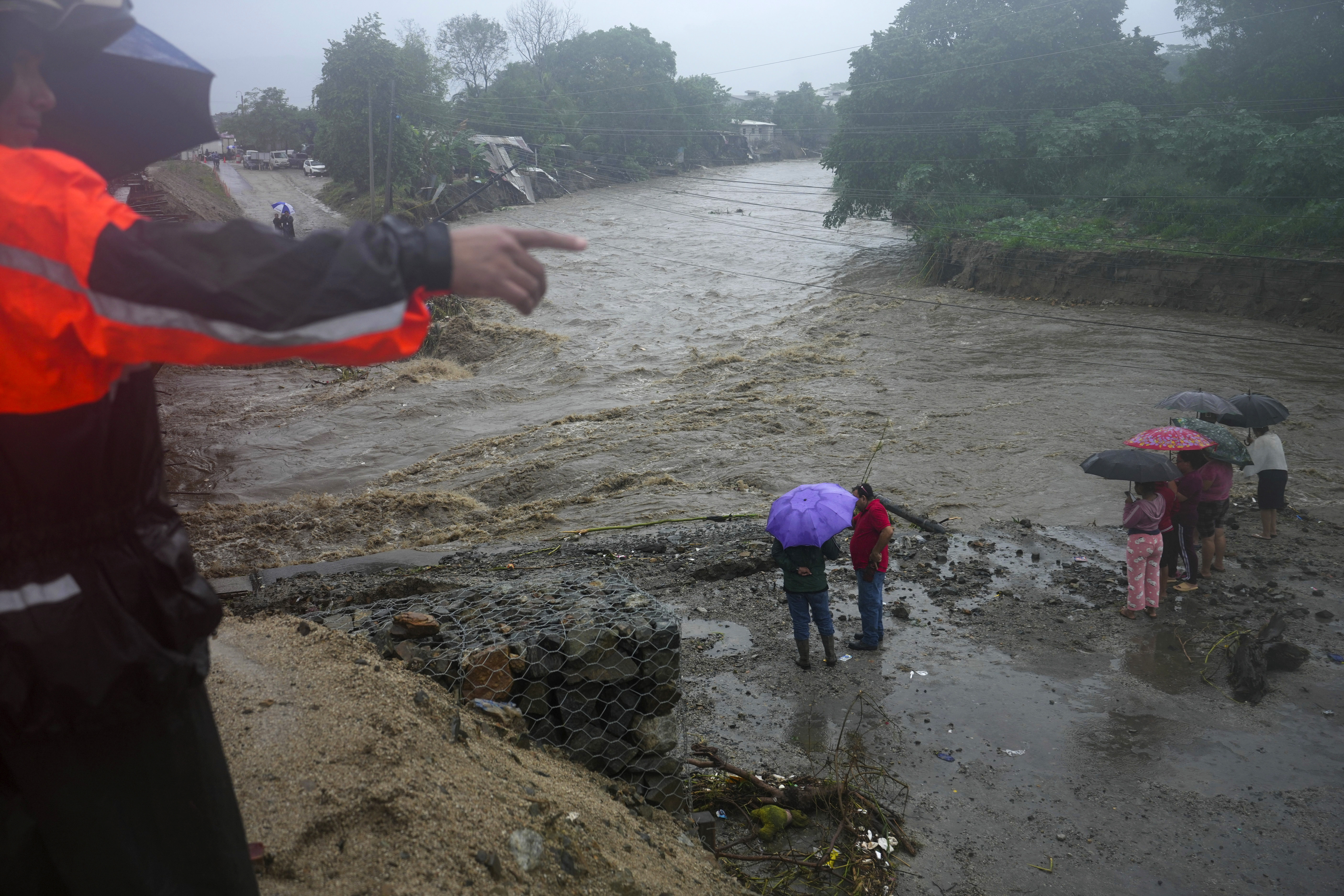 Residents stand alongside the banks of a river overrun by rains brought on by Tropical Storm Sara, on the outskirts of San Pedro Sula, Honduras, Saturday, Nov. 16, 2024. (AP Photo/Moises Castillo)