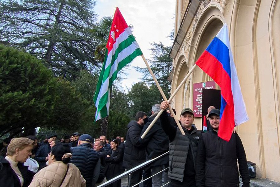 In this photo taken from video released by AIASHARA Independent Agency, Protesters, two of them hold an Abkhazian and Russian flags, gather outside the parliament building of the Georgian separatist region of Abkhazia as tensions flared over a proposed pact that would allow Russians to buy apartments in the region, Georgia, on Friday, Nov. 15, 2024, (AIASHARA Independent Agency via AP)