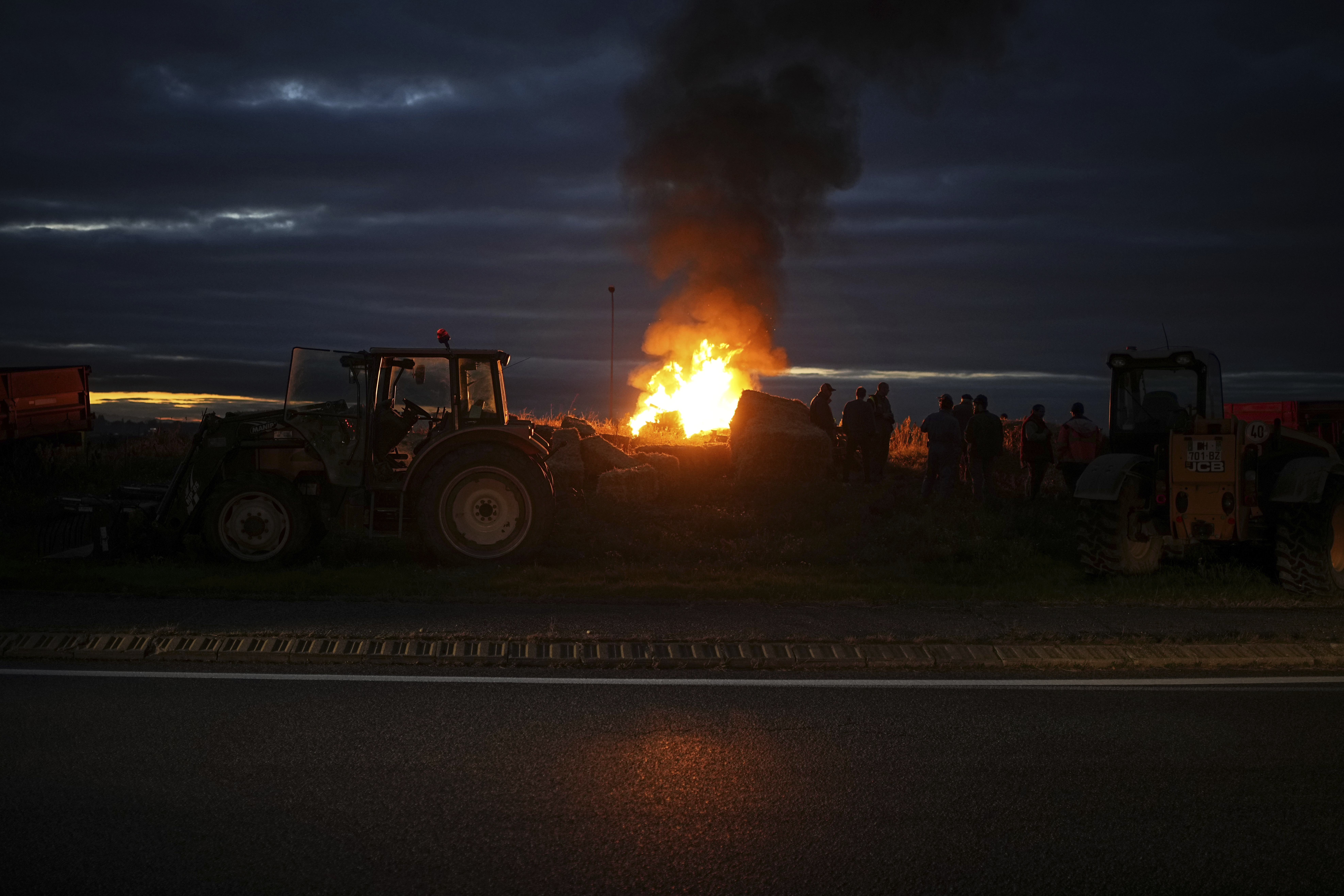 Farmers gather around a fire to protest against the EU-Mercosur trade agreement, in Saint-Laurent-de-Mure, near Lyon, central France, Monday, Nov. 18, 2024. (AP Photo/Laurent Cipriani)