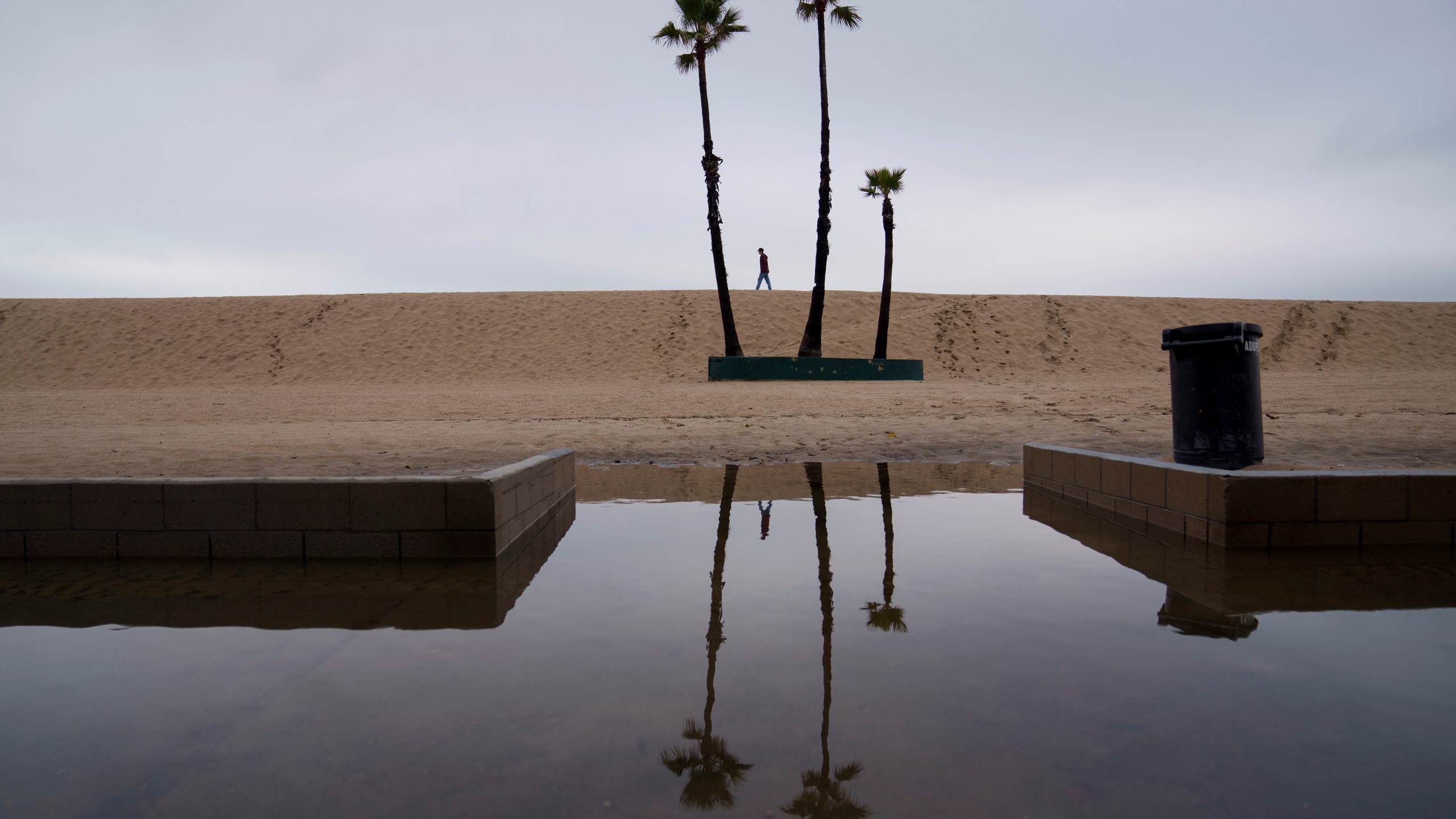 FILE - A person walks along the beach with flooding along the boardwalk Thursday, Feb. 1, 2024 in Seal Beach, Calif. (AP Photo/Eric Thayer, file)