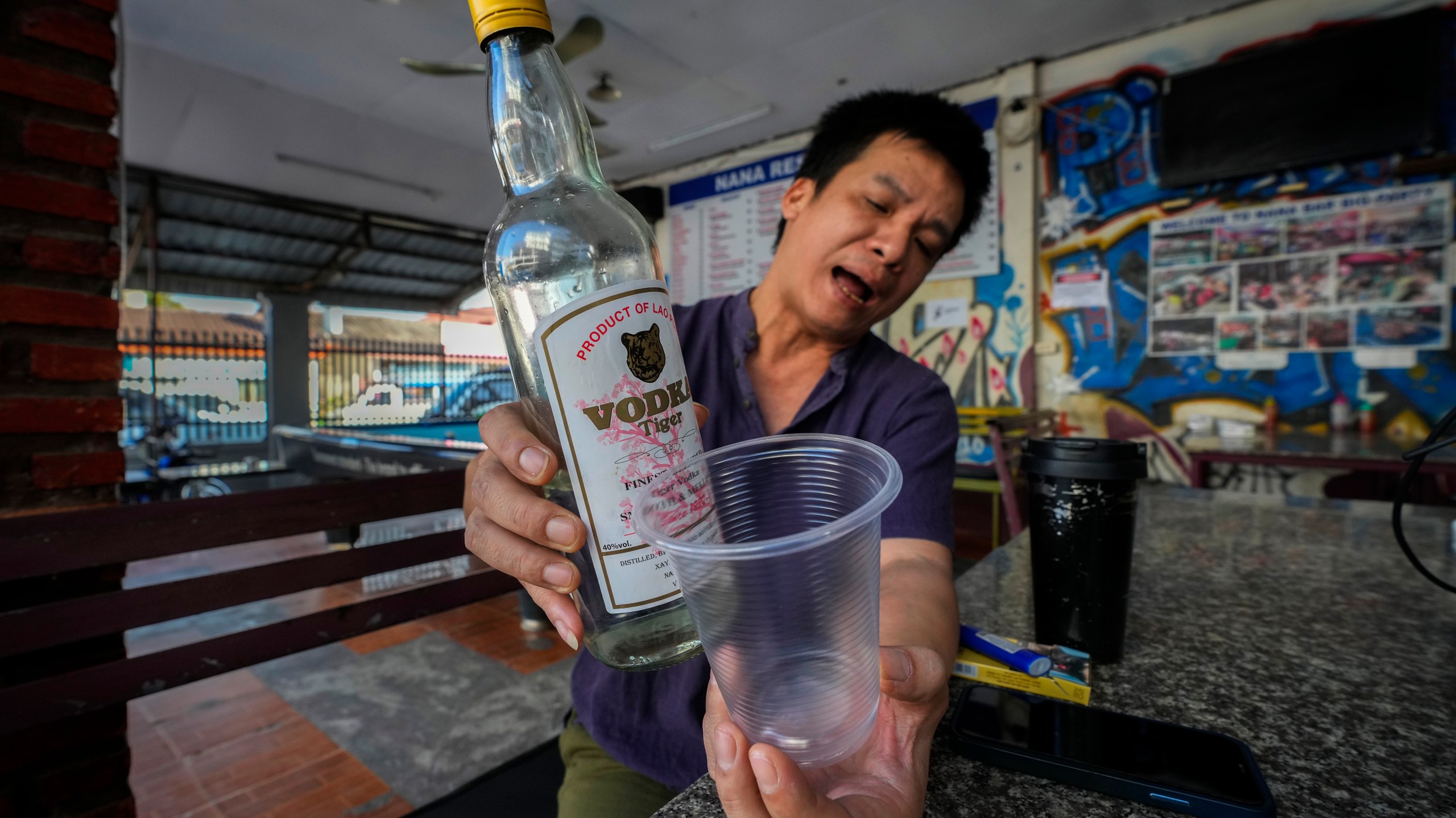 Duong Duc Toan, the manager of Nana Backpack hostel displays a bottle of vodka, in the bar of the hostel in Vang Vieng, Laos, Tuesday, Nov. 19, 2024. (AP Photo/Anupam Nath)