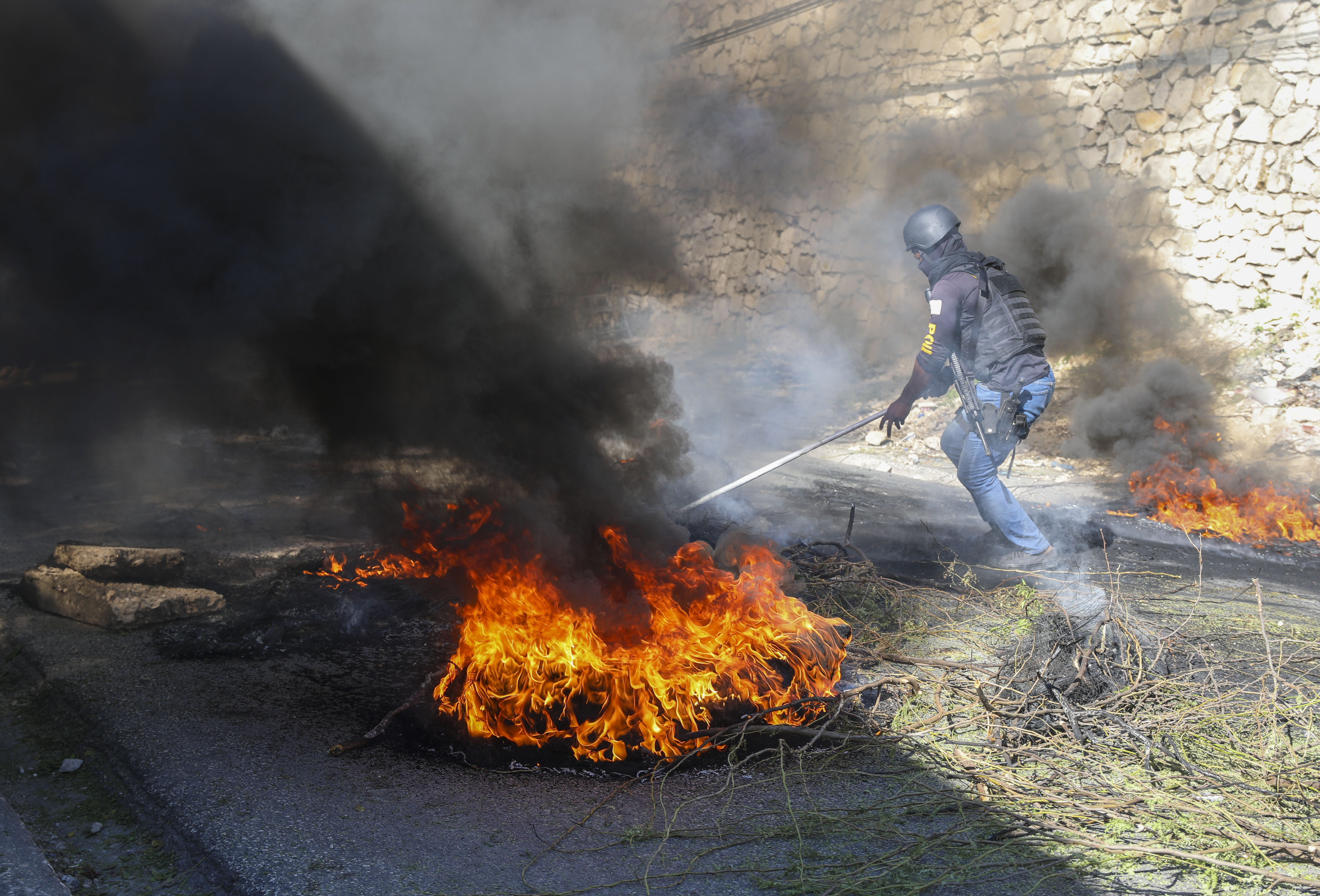 A police officer works to clear barricades of burning tires set on fire by residents to deter gang members from entering their neighborhood, in Port-au-Prince, Haiti, Tuesday, Nov. 19, 2024. (AP Photo/Odelyn Joseph)