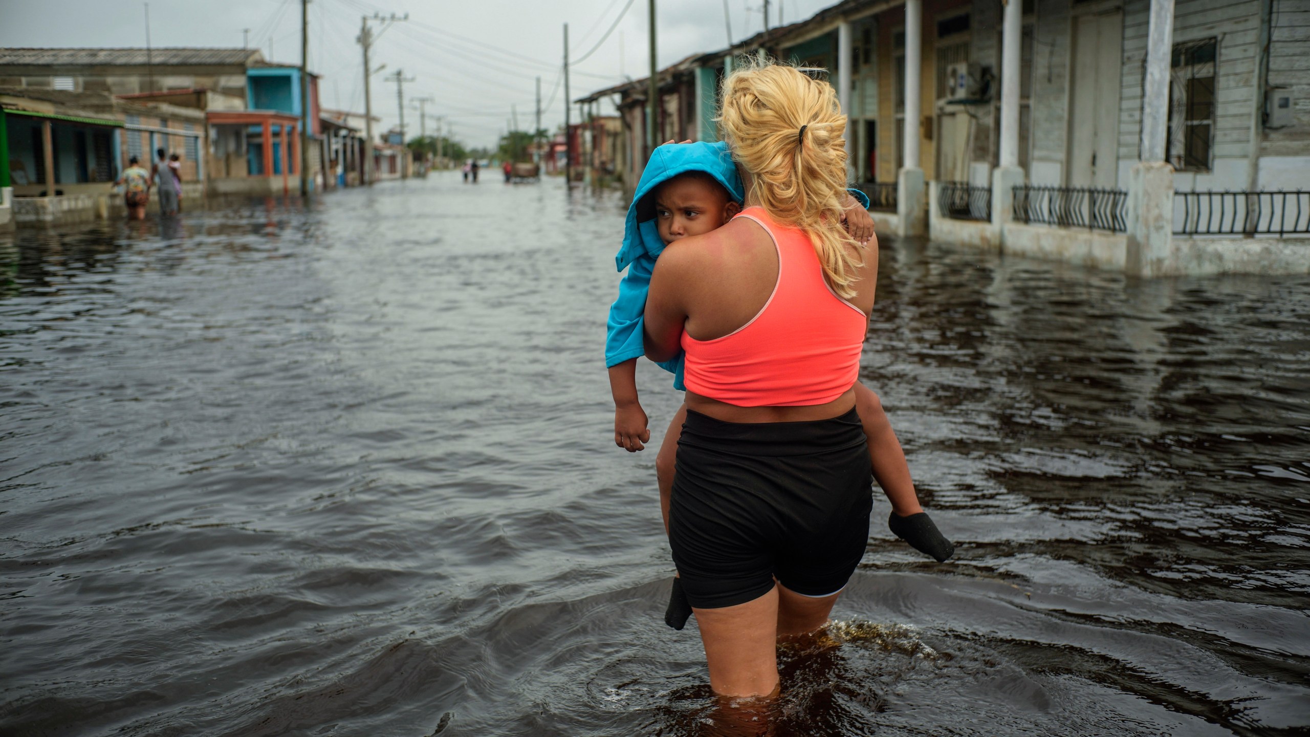 FILE - A woman carries a child as she wades through a street flooded in the passing of Hurricane Helene, in Batabano, Mayabeque province, Cuba, Sept. 26, 2024. (AP Photo/Ramon Espinosa, File)