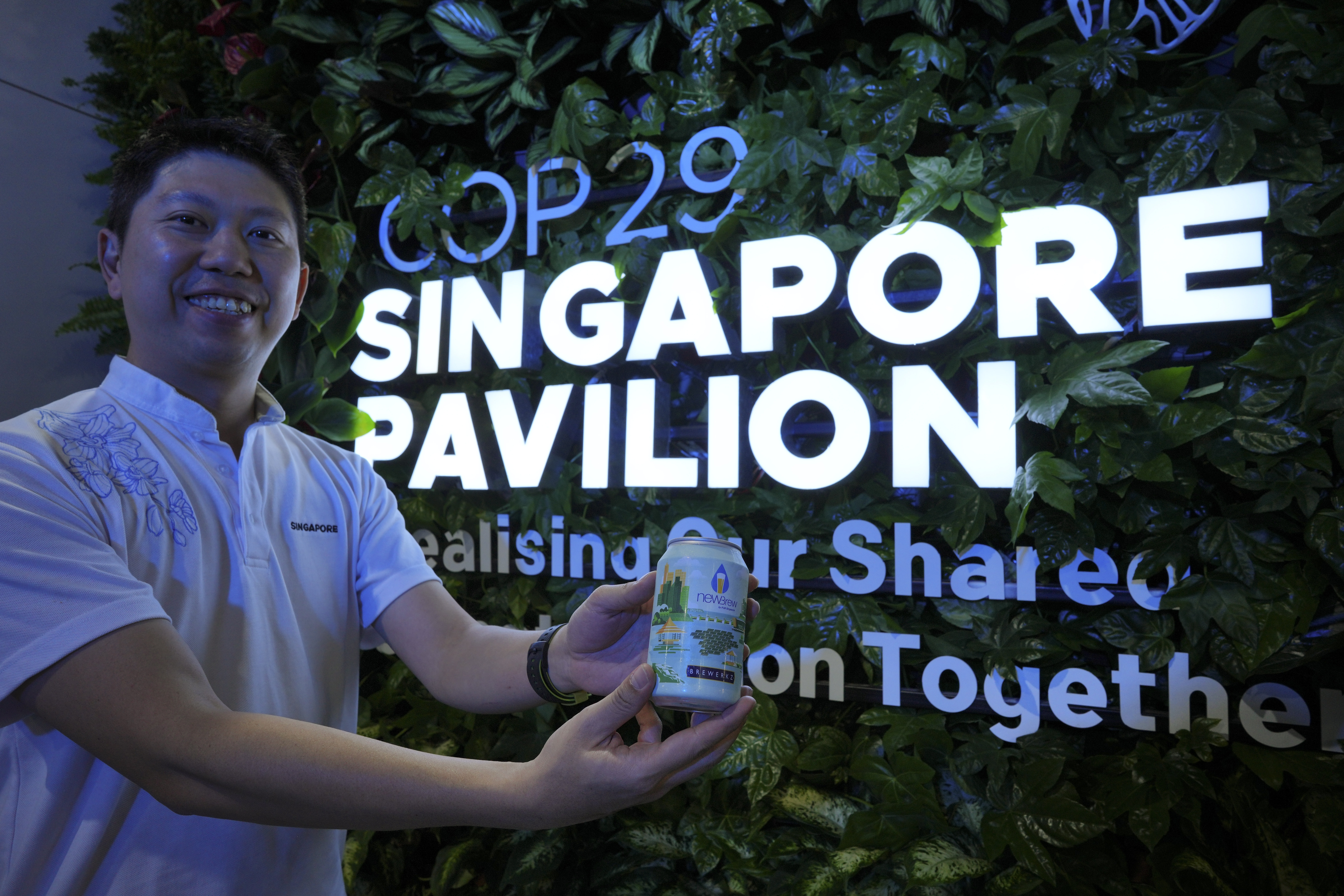 Nick Chow, part of the COP29 Singapore Pavilion team, poses for a photo with NEWBrew, beer made with treated wastewater, during the COP29 U.N. Climate Summit, Friday, Nov. 15, 2024, in Baku, Azerbaijan. (AP Photo/Peter Dejong)