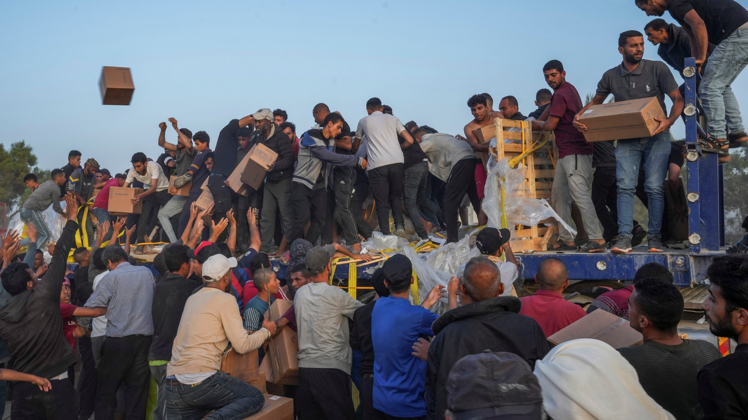 FILE - Palestinians storm trucks loaded with humanitarian aid brought in through a new U.S.-built pier, in the central Gaza Strip, on May 18, 2024. (AP Photo/Abdel Kareem Hana, File)