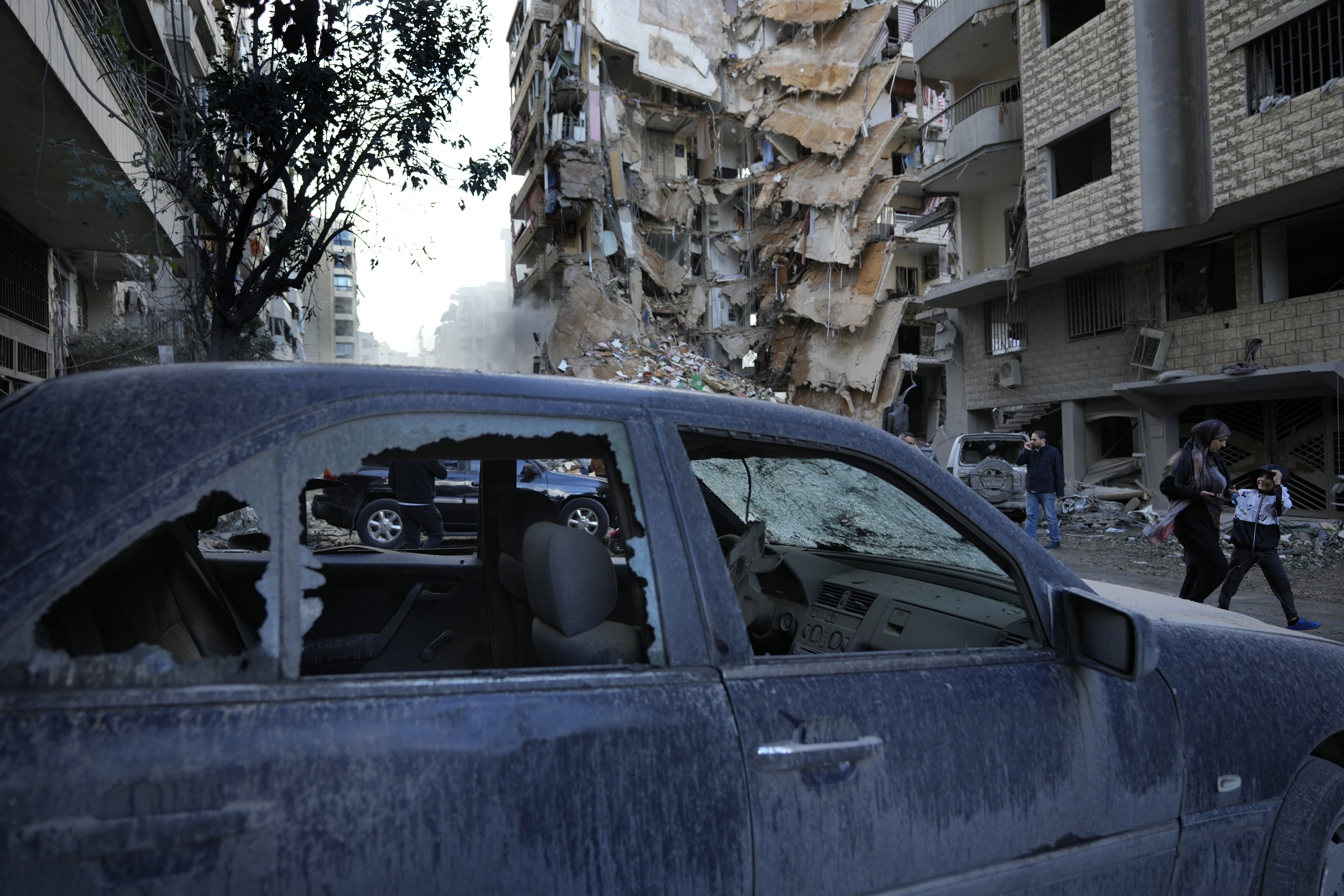 Residents pass in front of a destroyed building that was hit Sunday night in an Israeli airstrike in Dahiyeh, in the southern suburb of Beirut, Lebanon, Monday, Nov. 25, 2024. (AP Photo/Hussein Malla)