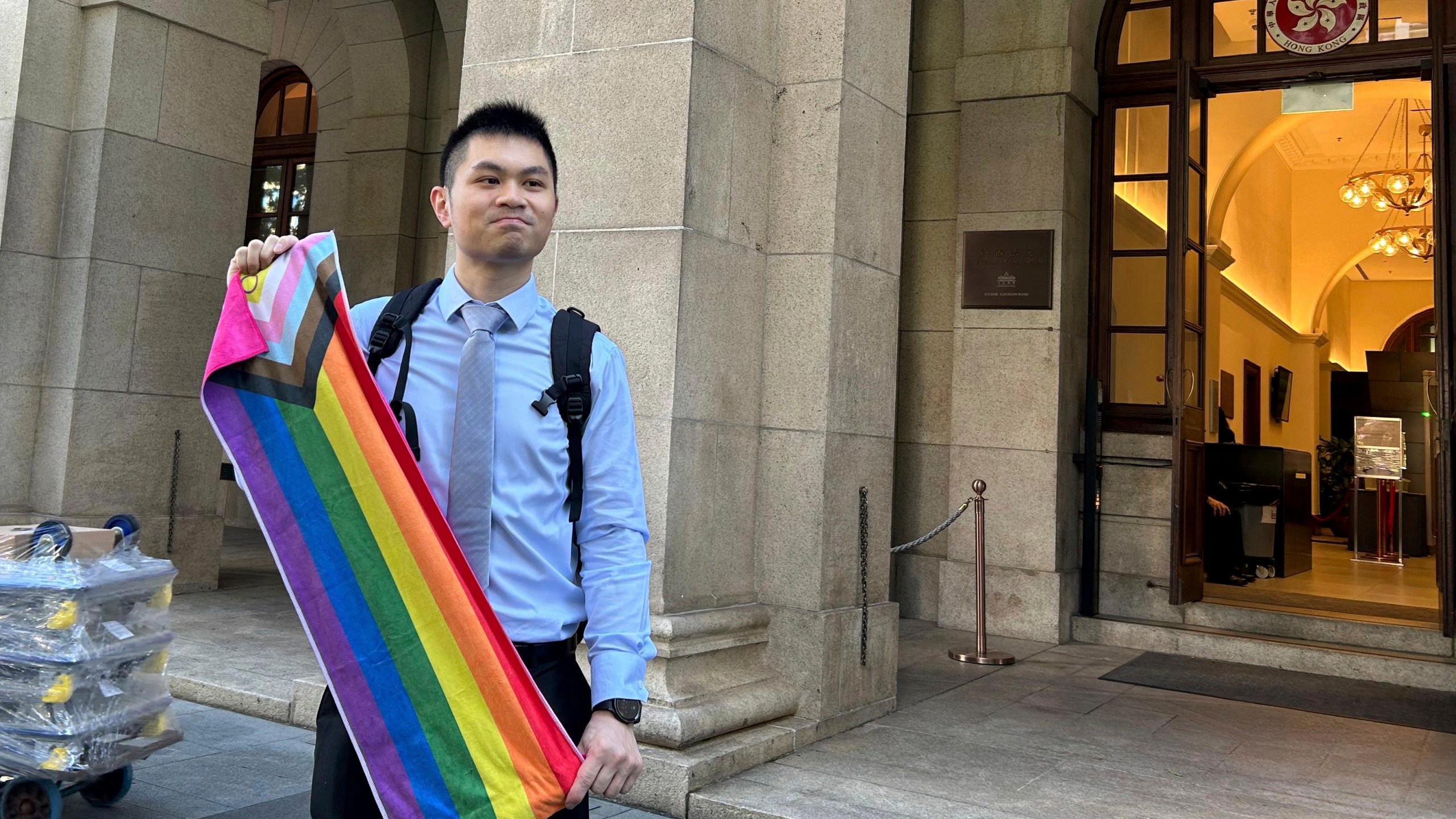 Nick Infinger, who won a years-long legal battle over the differential treatment facing same-sex couples, holds up a rainbow banner after speaking to media members outside Hong Kong’s top court on Tuesday, Nov. 26, 2024. (AP Photo/Kanis Leung)