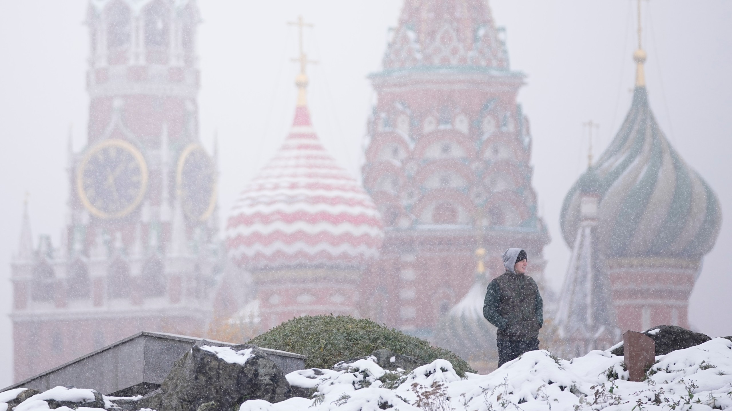 A man walks at Zaryadye park with the Spasskaya tower of the Kremlin and St. Basil's Cathedral in the background during a snowfall in Moscow, Russia, Wednesday, Nov. 6, 2024. (AP Photo/Pavel Bednyakov)