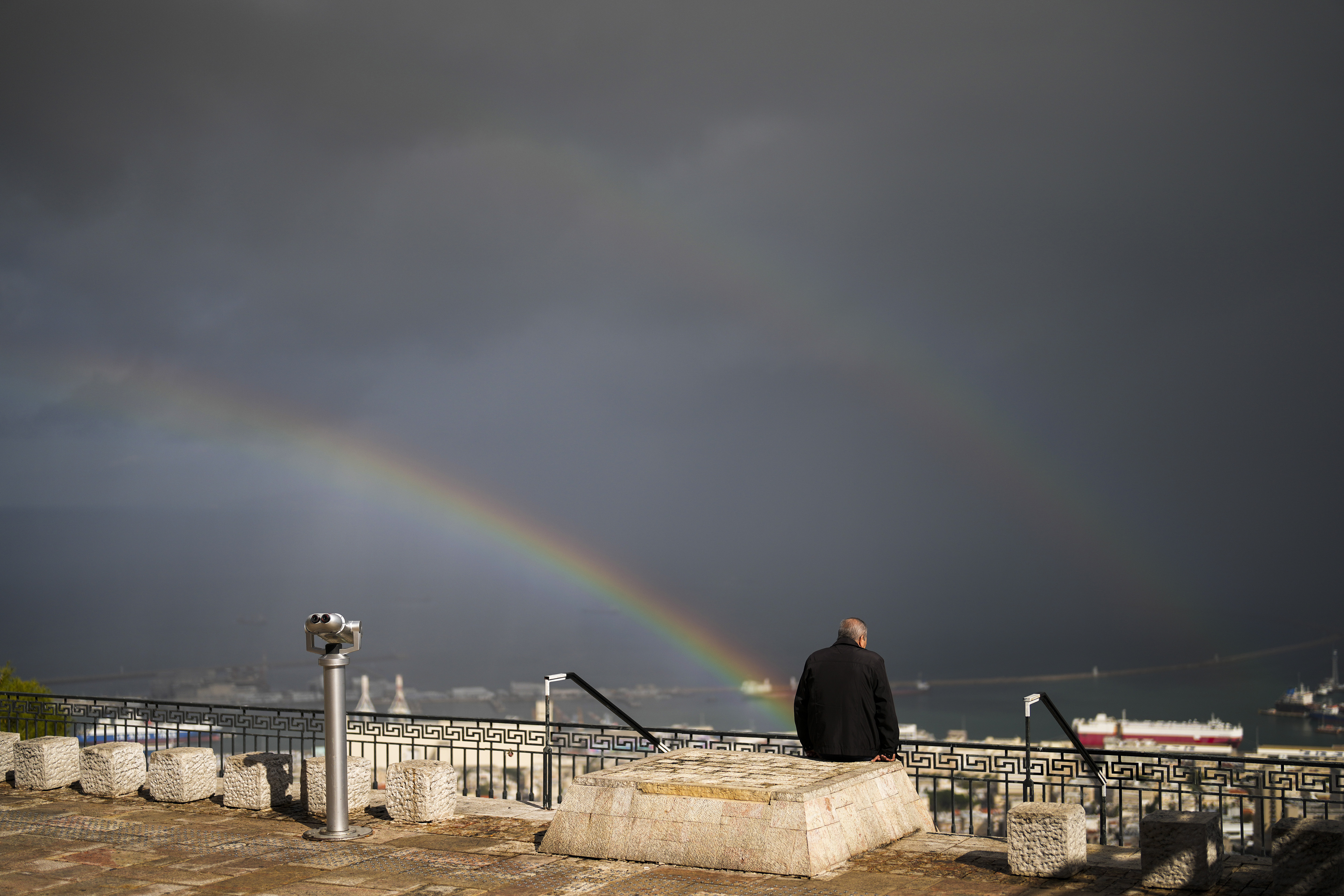 A double rainbow stretches across the sky as a man sits at a promenade overlooking Haifa, Israel, Tuesday, Nov. 26, 2024. (AP Photo/Francisco Seco)