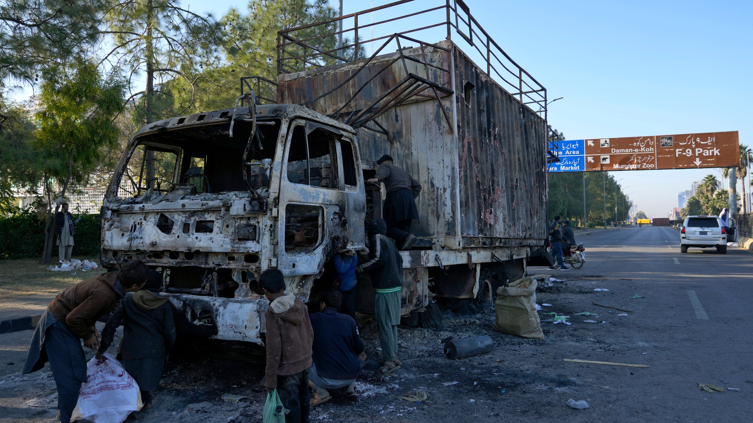 Scavengers look useful stuff from a burnt container which was used by leaders of imprisoned former Prime Minister Imran Khan's Pakistan Tehreek-e-Insaf party for speech and left behind when security forces launched an operation Tuesday night to disperse them, in Islamabad, Pakistan, Wednesday, Nov. 27, 2024. (AP Photo/Anjum Naveed)