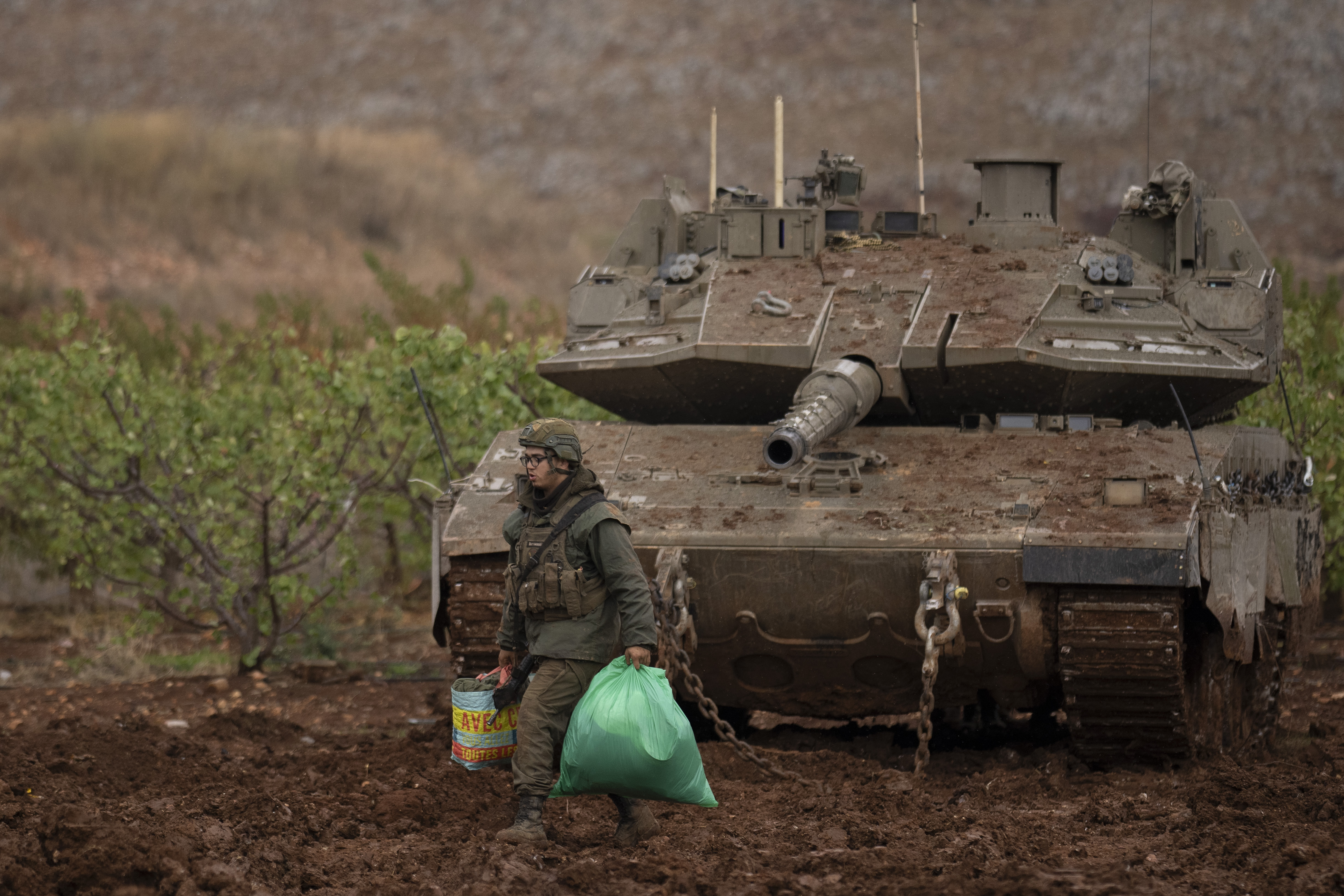 An Israeli soldier walks past a tank on an area near the Israeli-Lebanese border, as seen from northern Israel, Wednesday, Nov. 27, 2024. (AP Photo/Leo Correa)