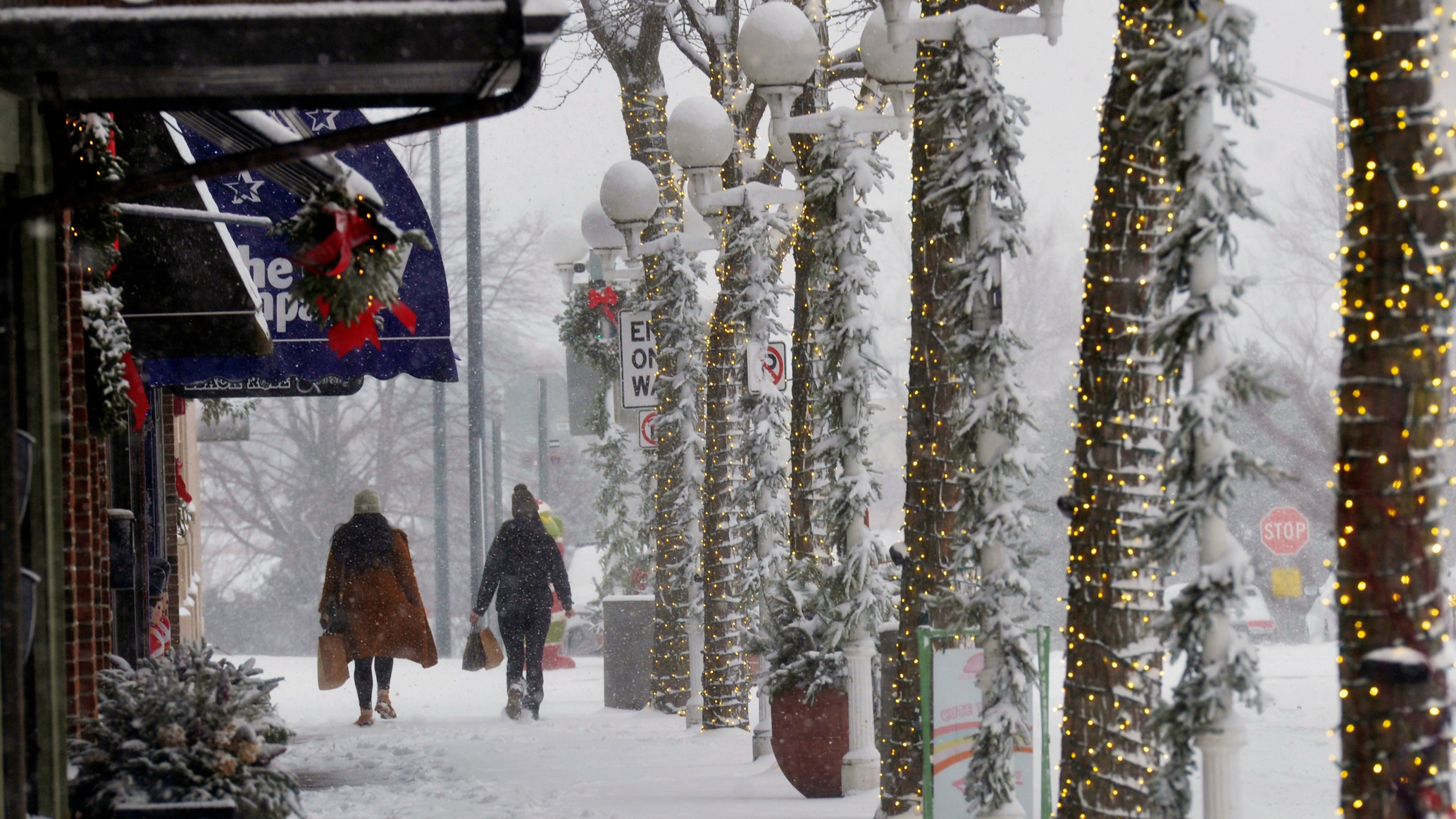 Shoppers walk through blowing and drifting snow, Monday, Dec. 2, 2024, in downtown St. Joseph, Mich. (Don Campbell/The Herald-Palladium via AP)